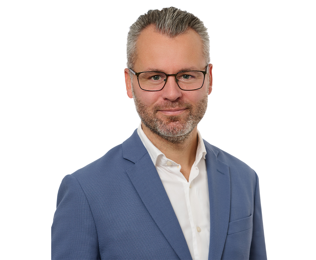 Porträttfoto av en man med glasögon och skägg, klädd i blå kavaj och vit skjorta.