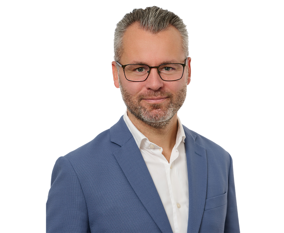 Porträttfoto av en man med glasögon och skägg, klädd i blå kavaj och vit skjorta.