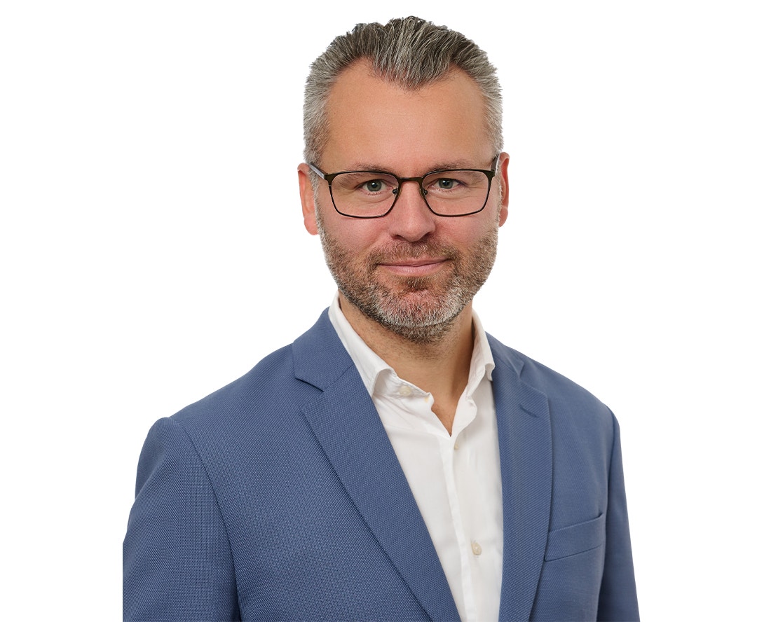 Porträttfoto av en man med glasögon och skägg, klädd i blå kavaj och vit skjorta.