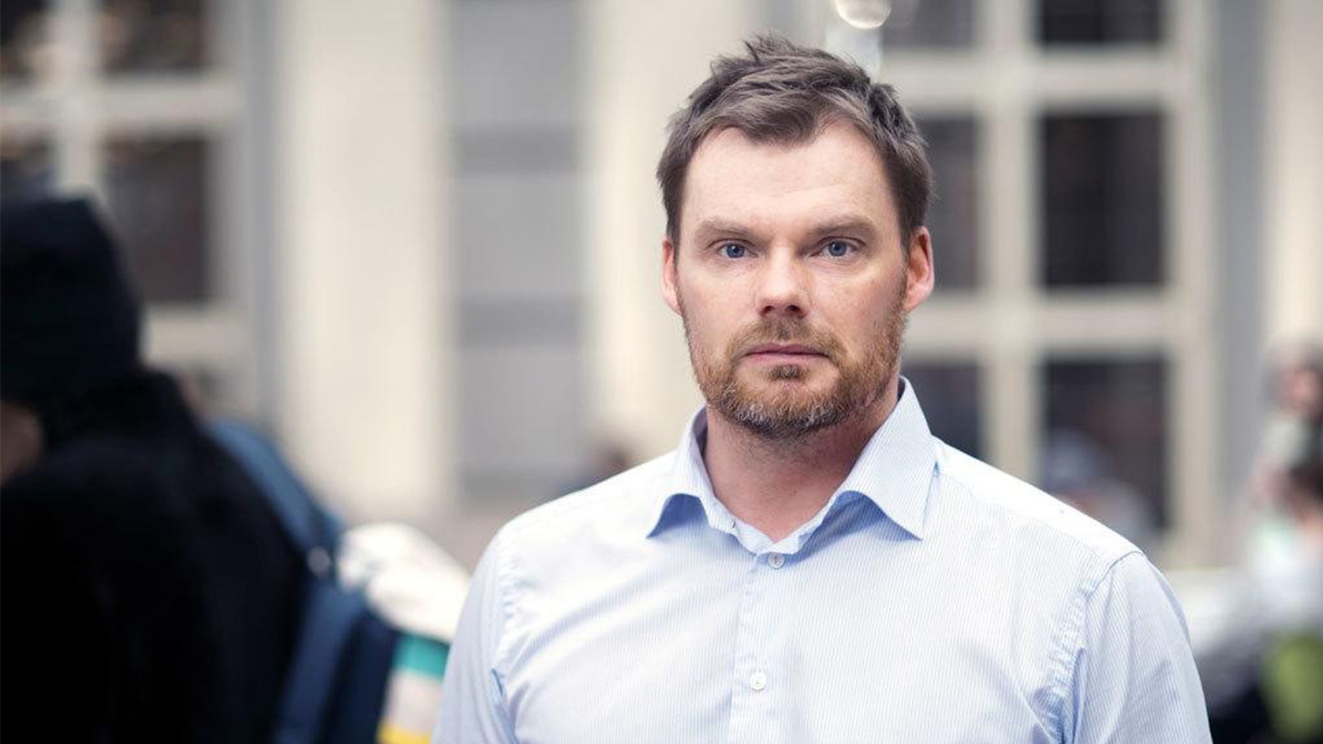 Rickard Sandberg poserar vid Handelshögskolan. Han bär blå skjorta och tittar seriöst in i kameran.