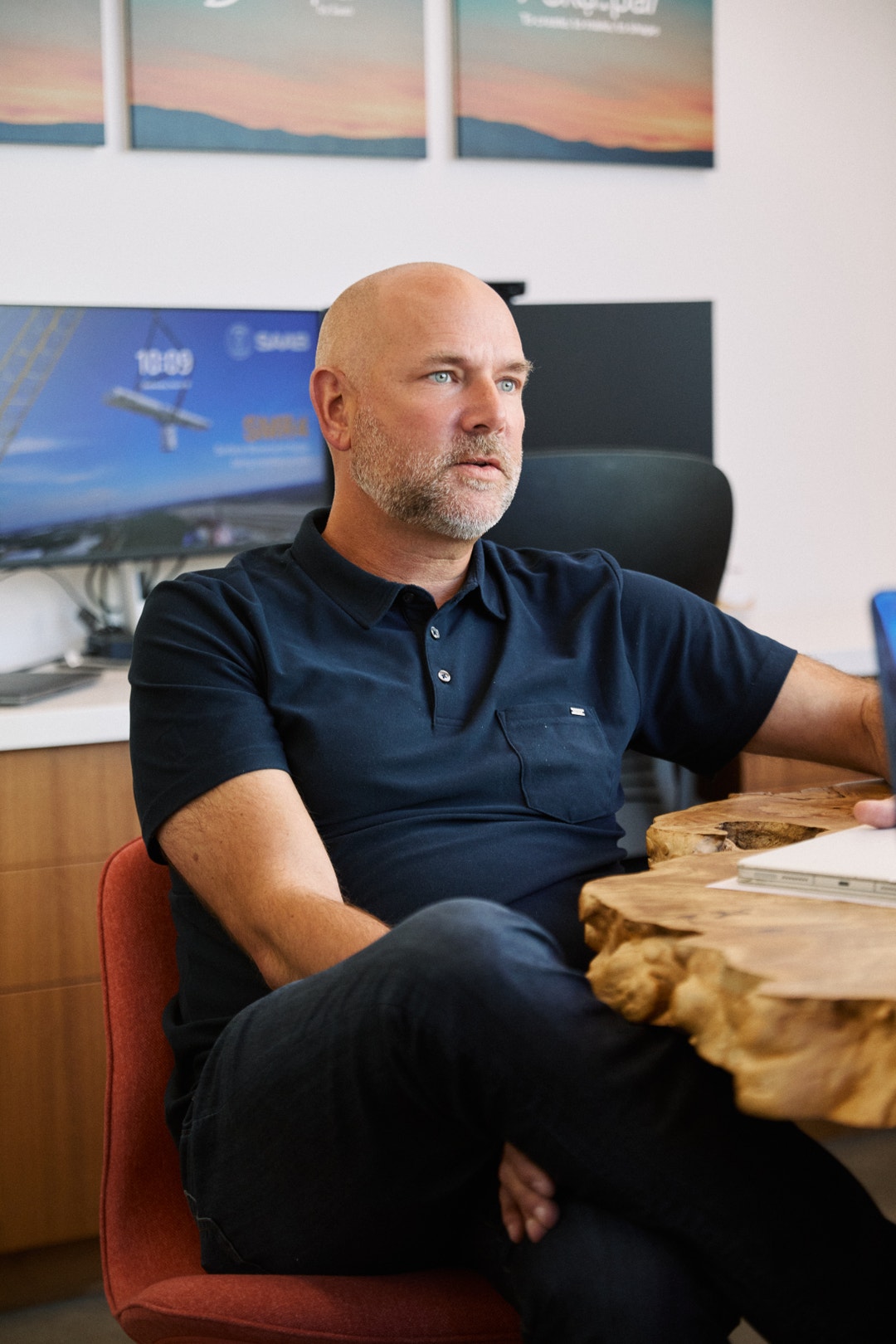 Man i mörk blå poloskjorta sitter vid ett skrivbord på ett kontor.