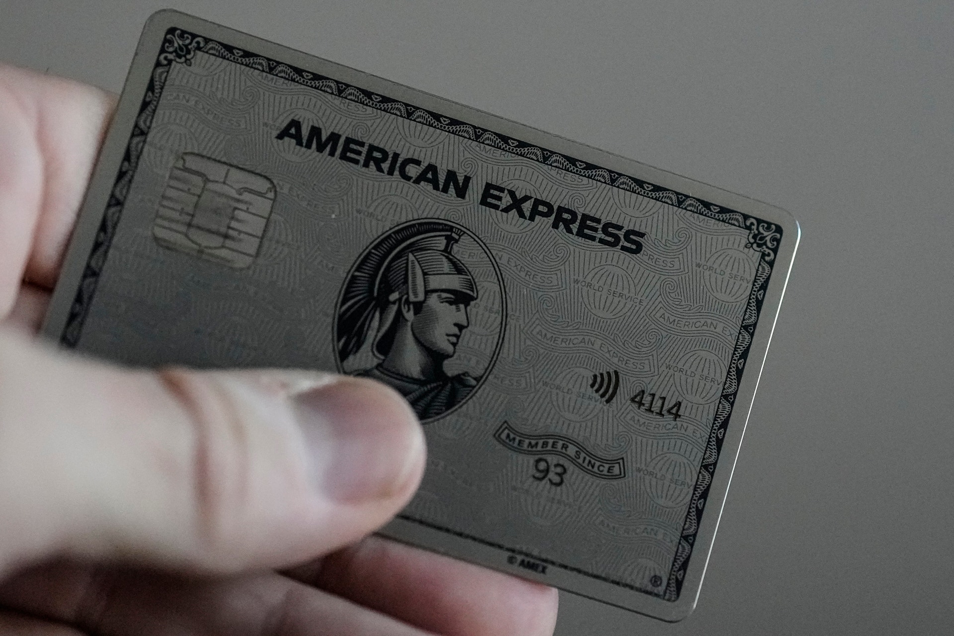 En hand som håller ett grått American Express-kort med metallfinish och det klassiska American Express-logotypen synlig.