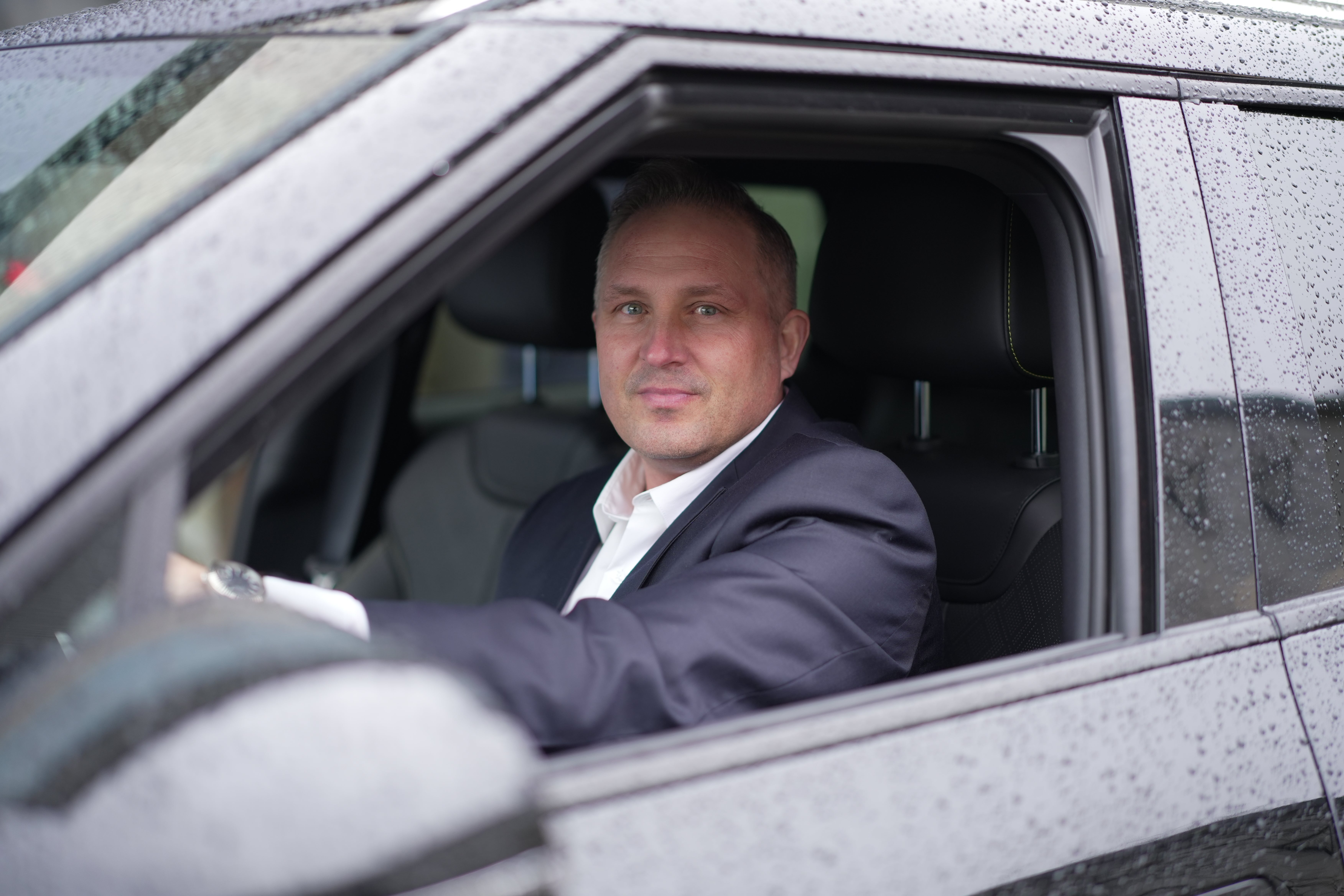 Man i kostym sitter bakom ratten i en bil