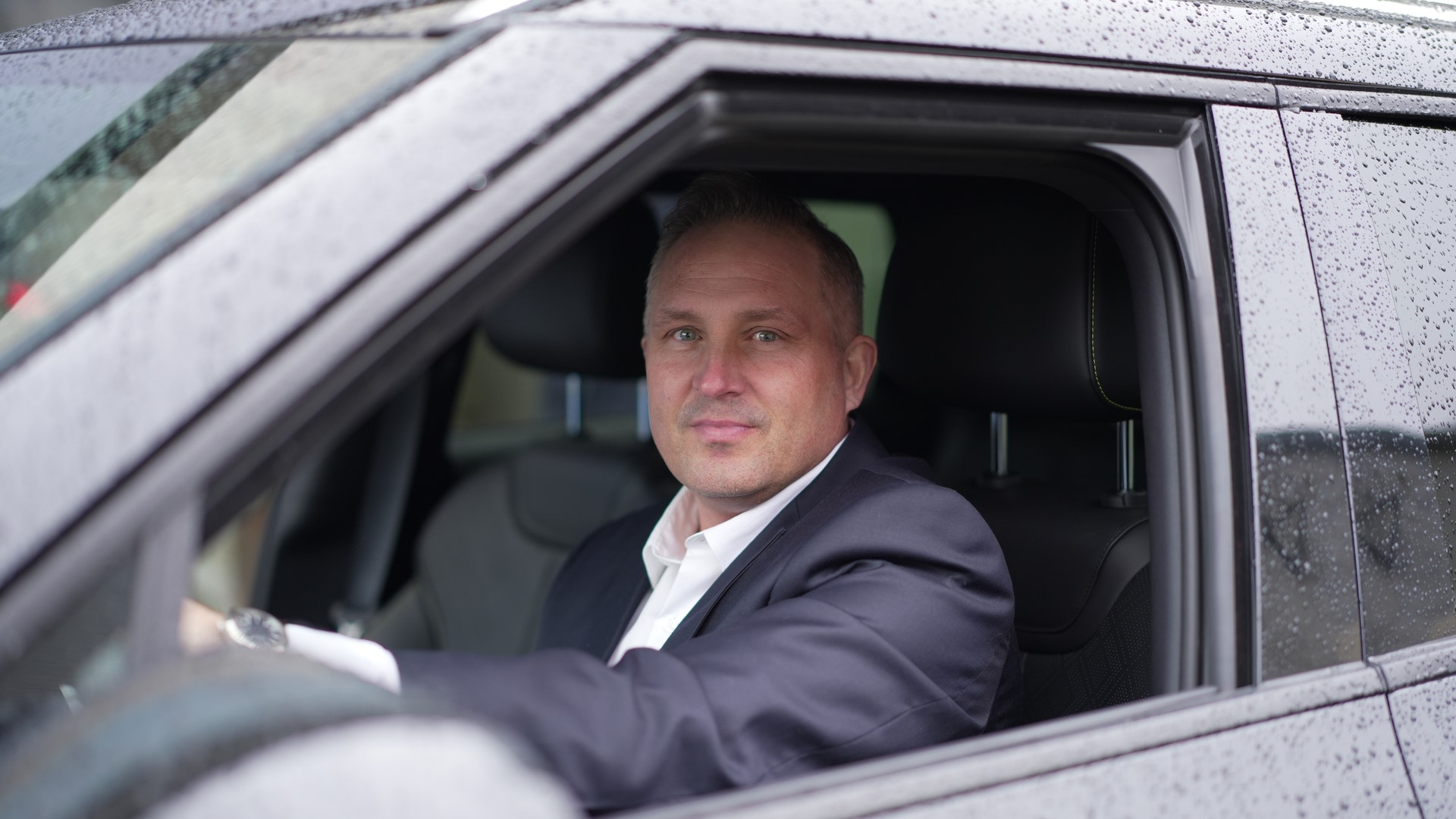 Man i kostym sitter bakom ratten i en bil