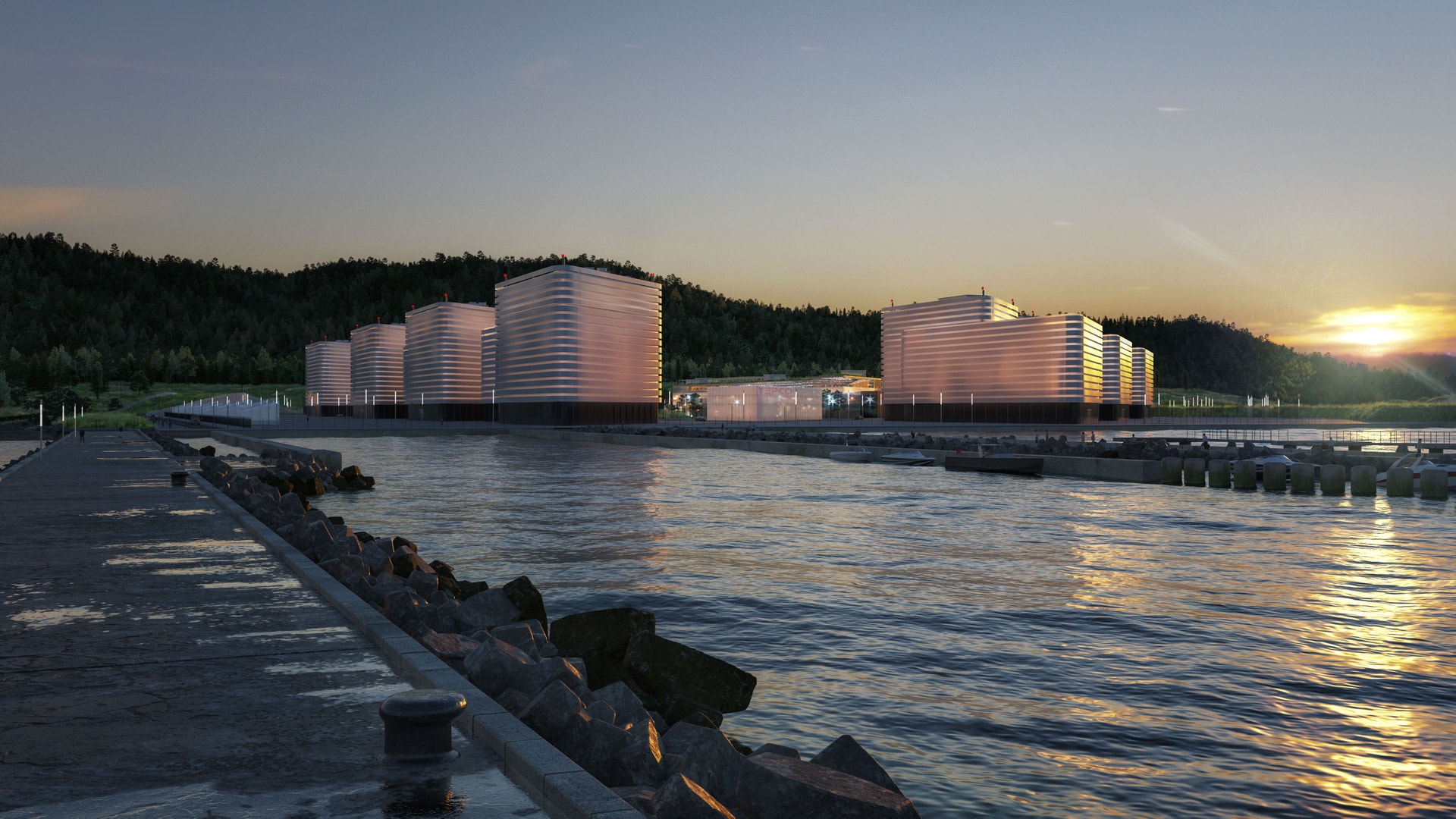 SMR Campus vid solnedgång. Moderna cylindriska byggnader belyst av gyllent solljus reflekteras i vattnet. Skog syns i bakgrunden.