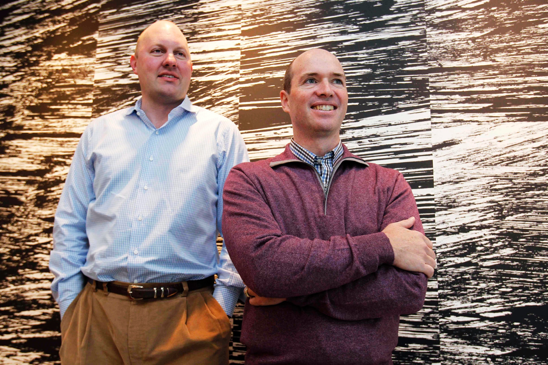 Två män står framför en trävägg och ler mot kameran.