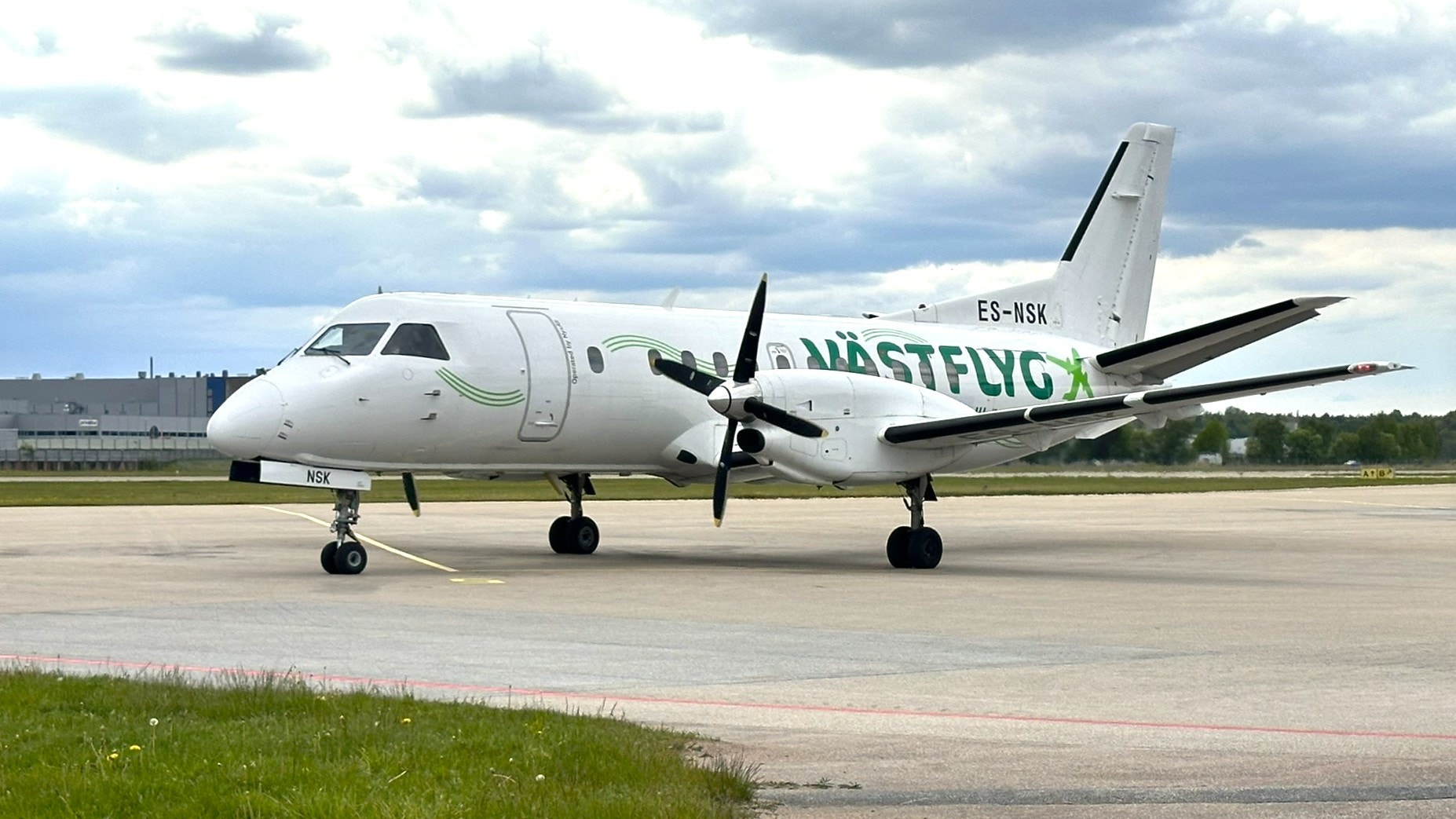 Ett vitt propellerflygplan från Widerøe står parkerat på en flygplats med molnig himmel i bakgrunden.