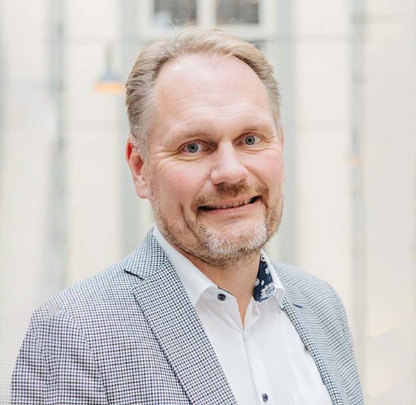 Porträttfoto av en man i business-casual kläder som ler mot kameran.