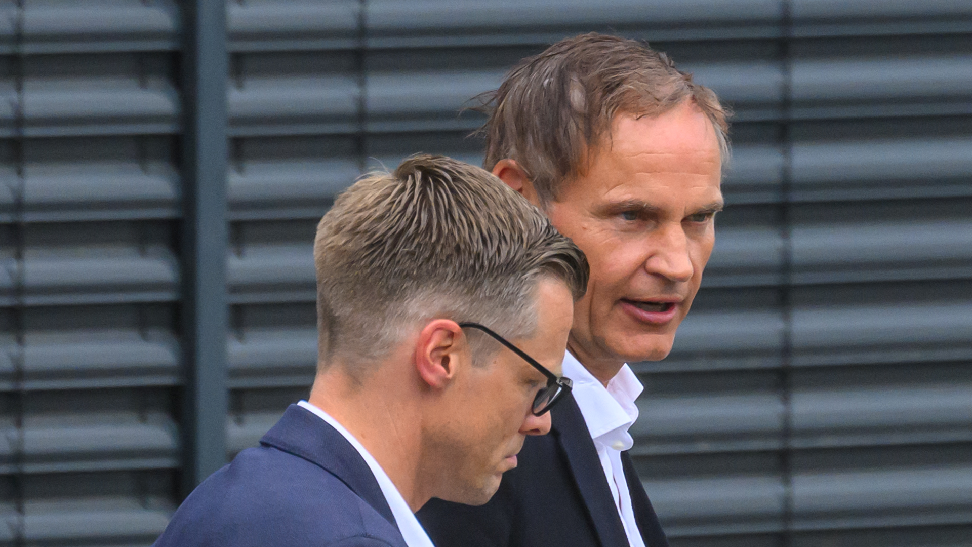 Två män i affärskläder står tillsammans framför en mörk vägg.
