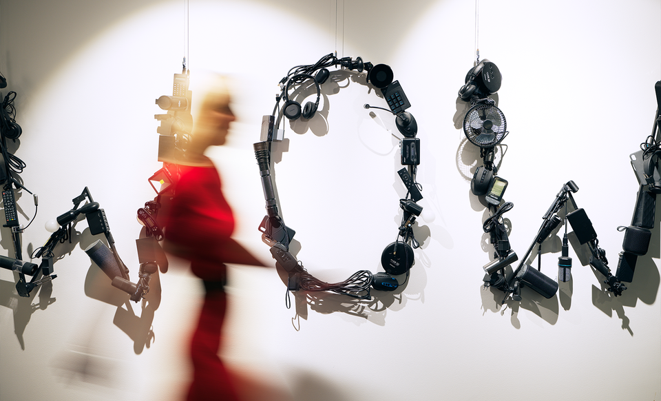 Kvinna i röd klänning går förbi hängande mekaniska armar och robotiska skulpturer på en vit vägg.