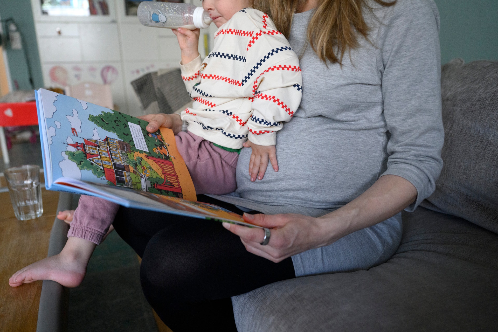 En vuxen person läser en färgglad barnbok tillsammans med ett litet barn på en soffa.