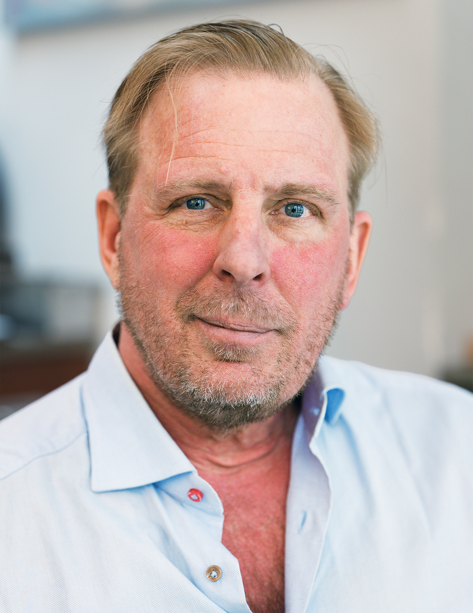 Porträttfoto av en man med ljust hår och blå ögon, klädd i ljusblå skjorta.