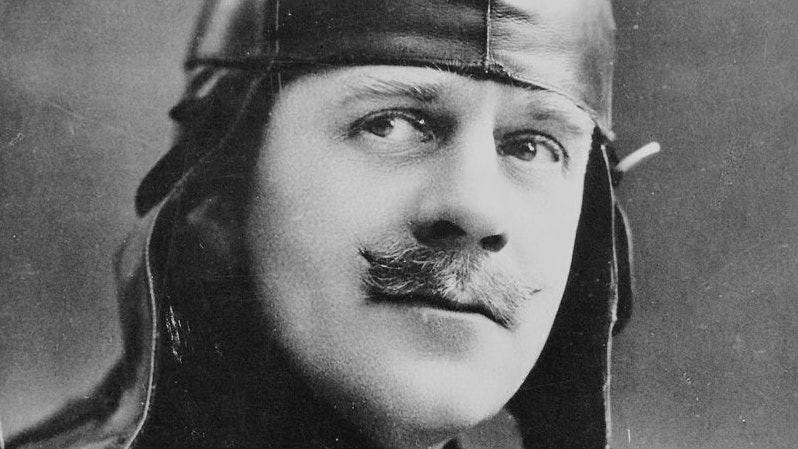 Svartvit porträttfotografi av en man med mustasch iklädd flygarhatt från tidigt 1900-tal.