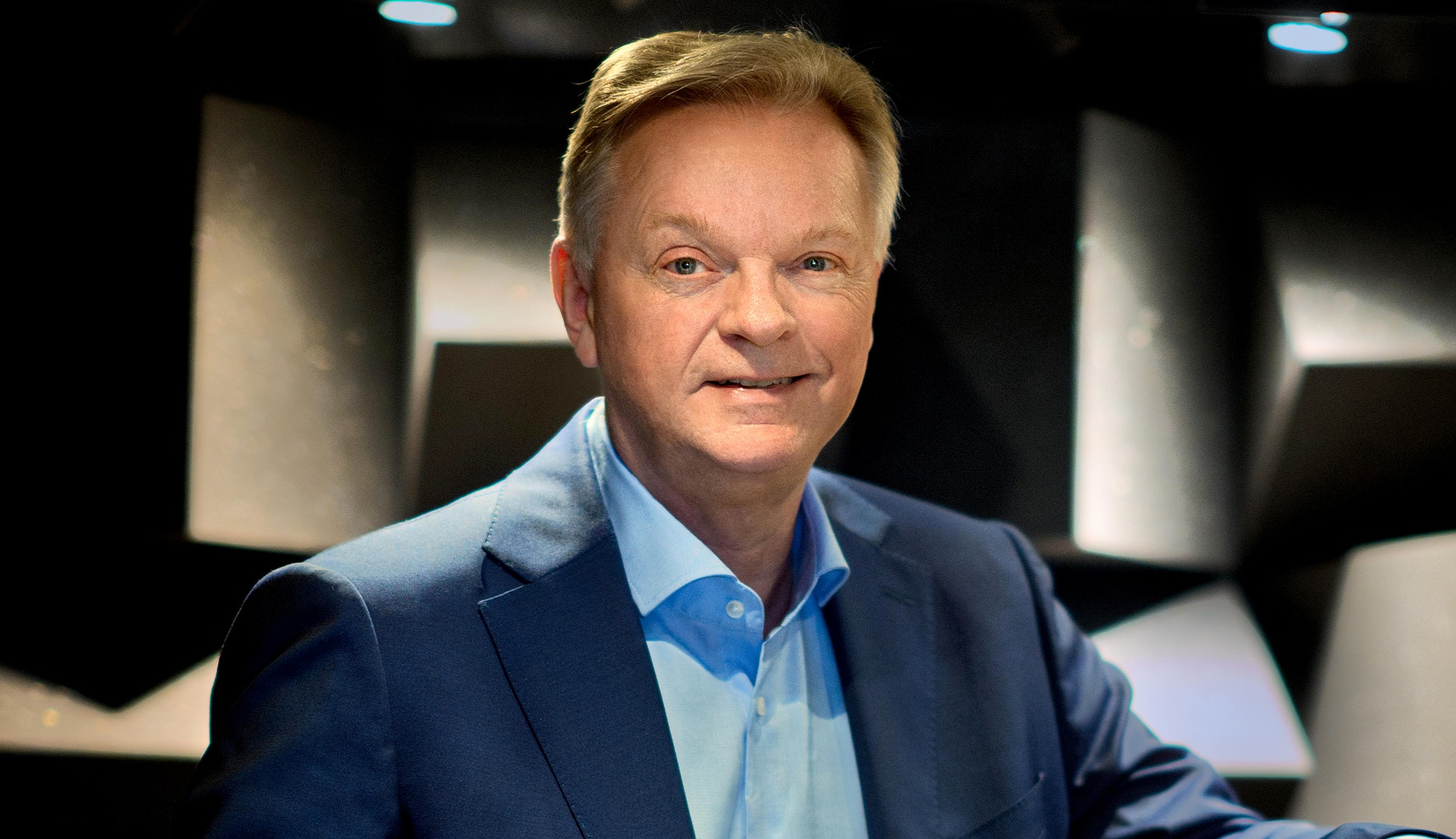 Porträttbild av en man i kostym som ler mot kameran i en tv-studio.