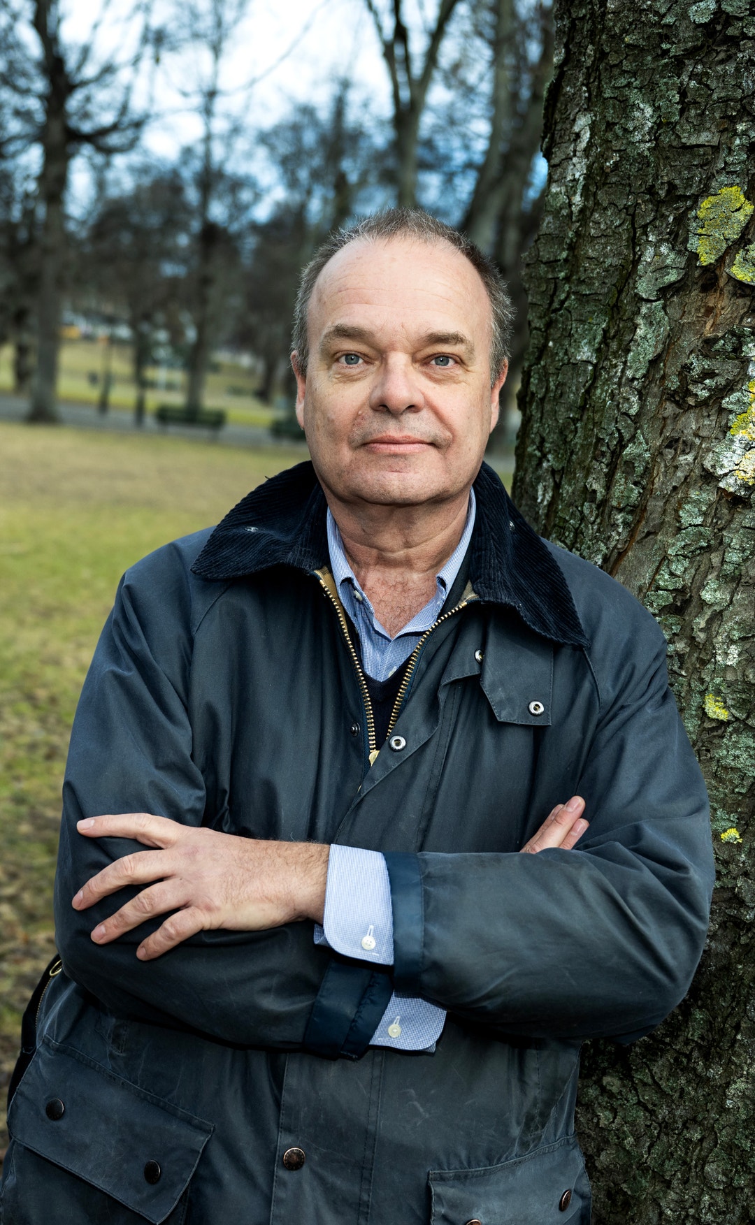 Porträtt av en man som står lutad mot ett träd i en park. Han är klädd i mörkblå jacka och har armarna i kors.
