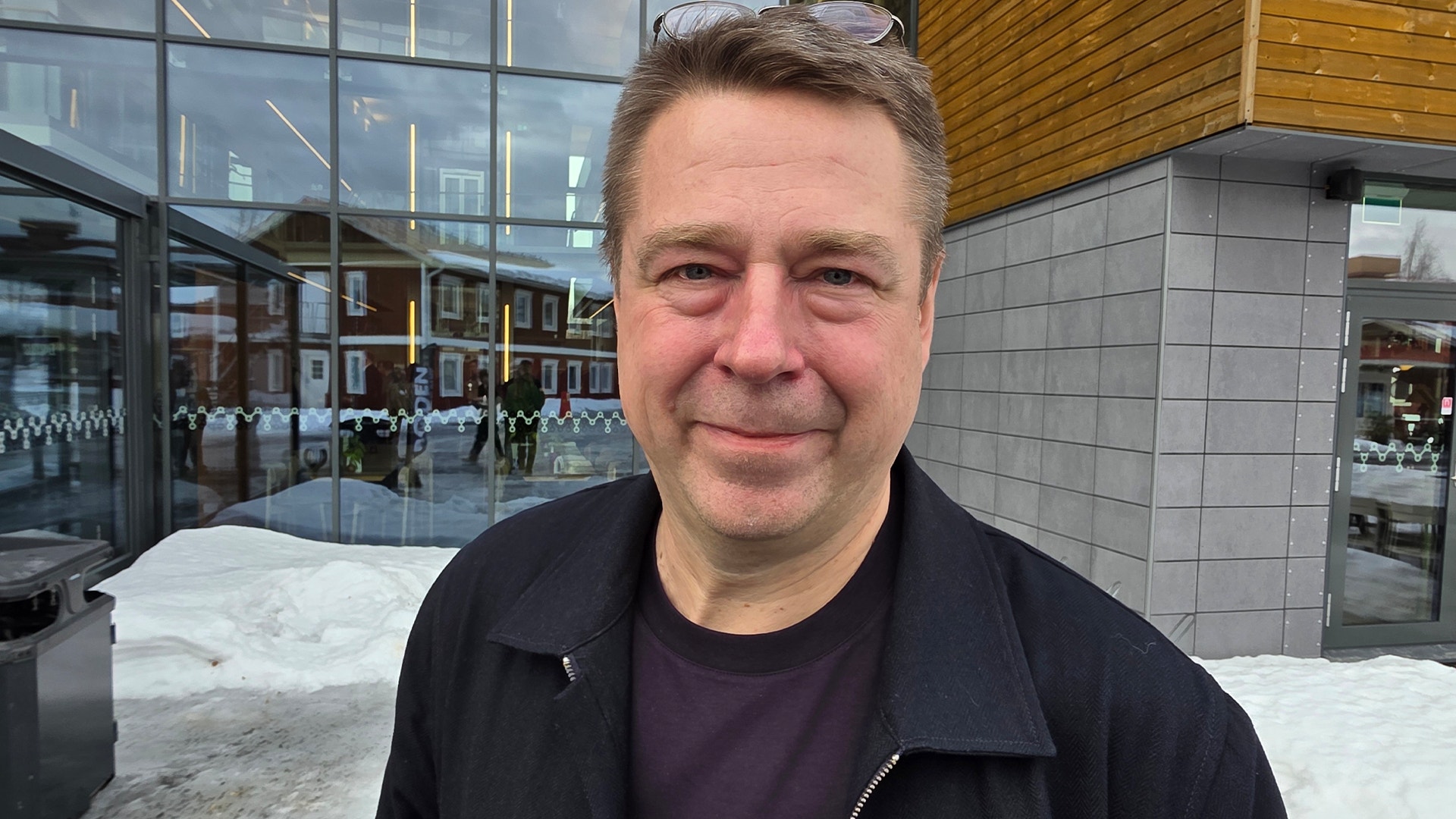 Porträtt av en man i svart jacka framför en modern byggnad i stadsmiljö