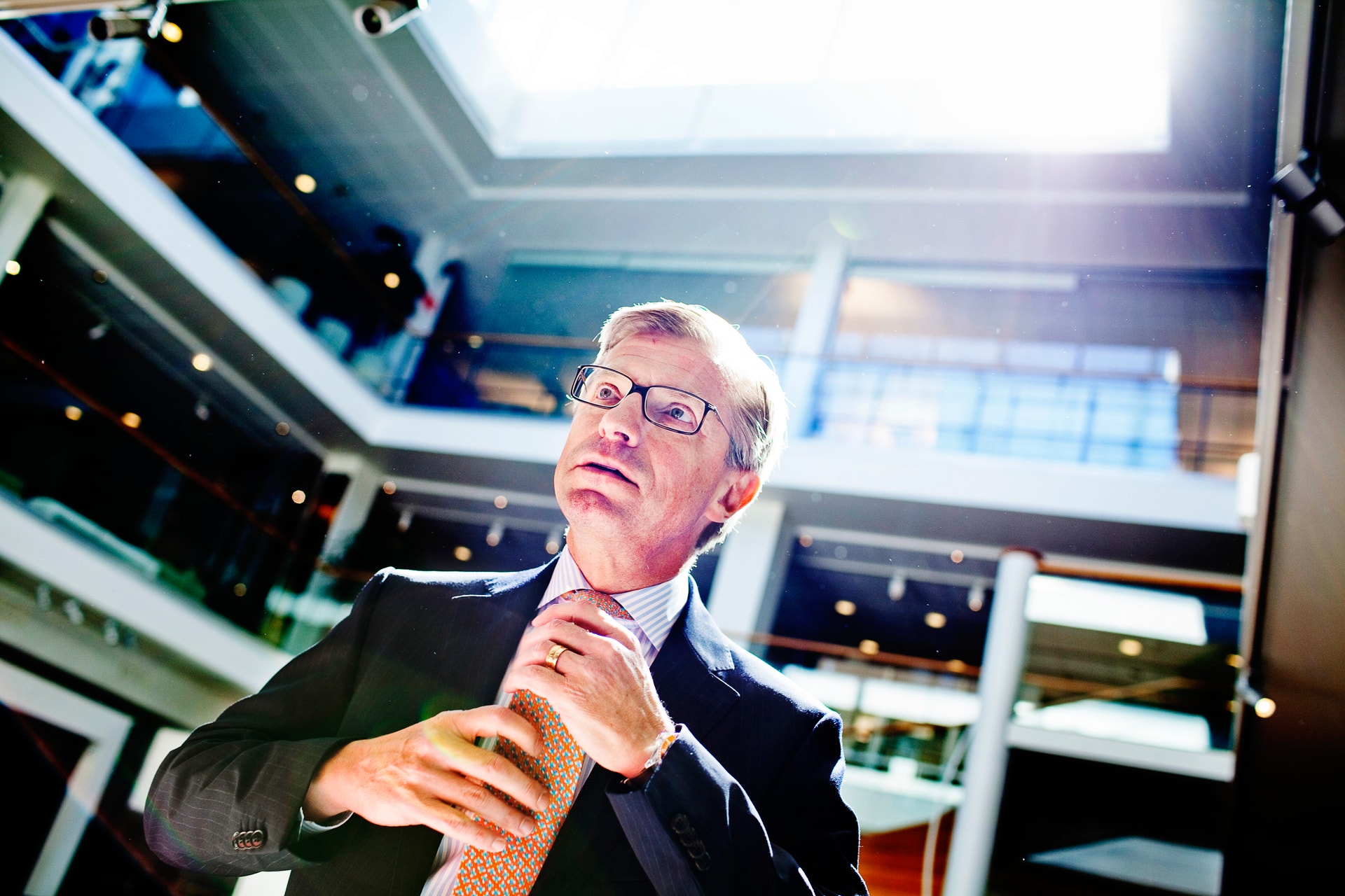 En man i affärskläder och glasögon står i en modern kontorsmiljö och gestikulerar medan han talar.