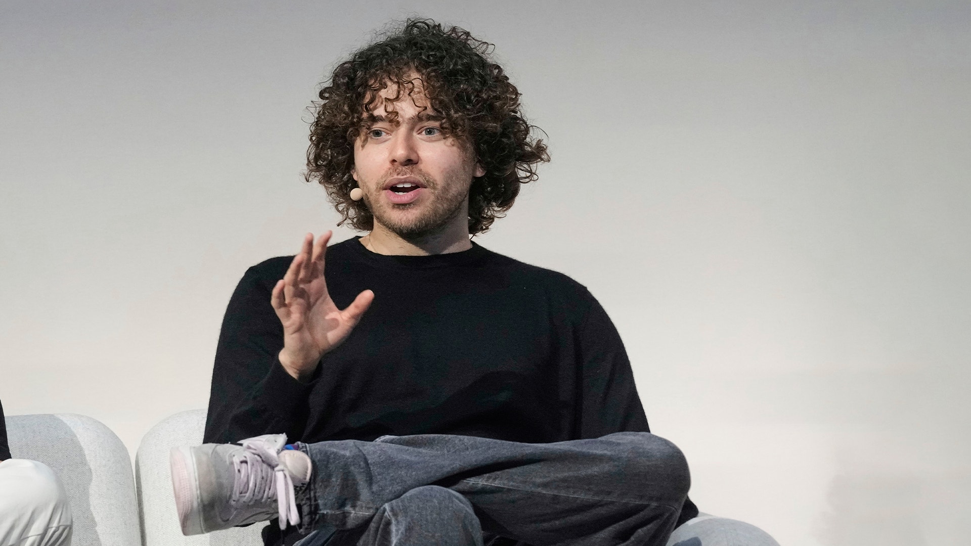 En man med lockigt mörkt hår sitter och gestikulerar medan han talar.