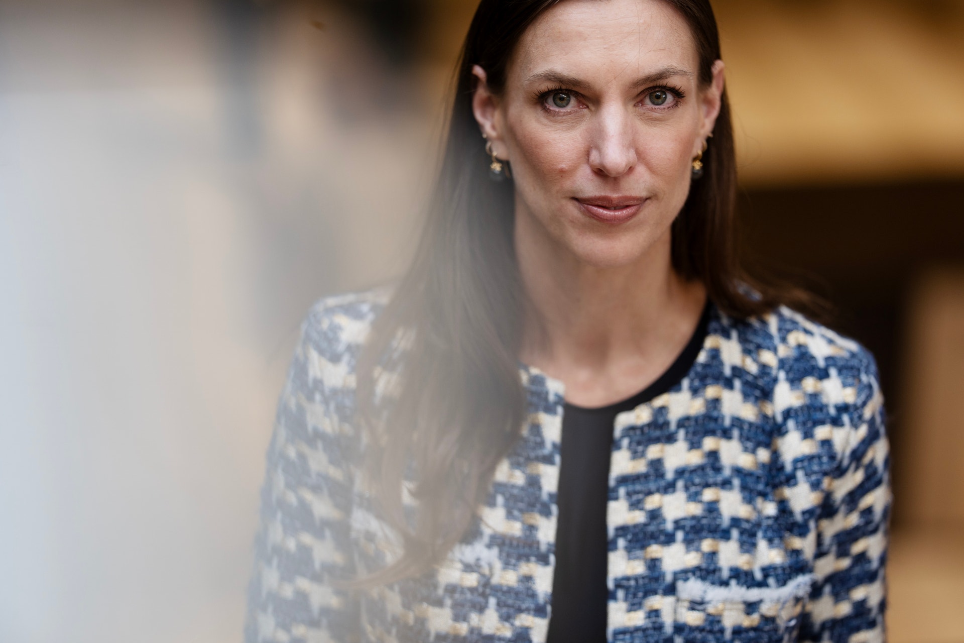 Porträtt av en kvinna med långt mörkt hår, iklädd en blå och vit mönstrad jacka över en svart topp.