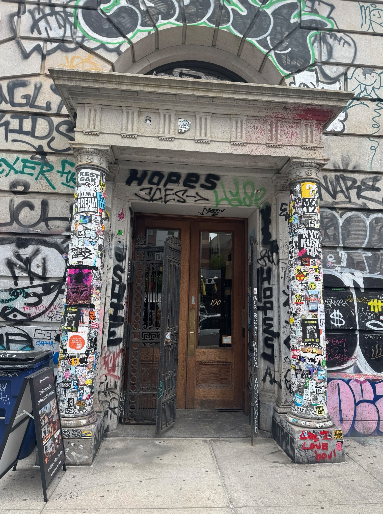 En bruntödd dörr till en byggnad helt täckt av färgglad graffiti och klistermärken. Vita pelare på båda sidor av dörren är också täckta av graffiti i olika färger och stilar.