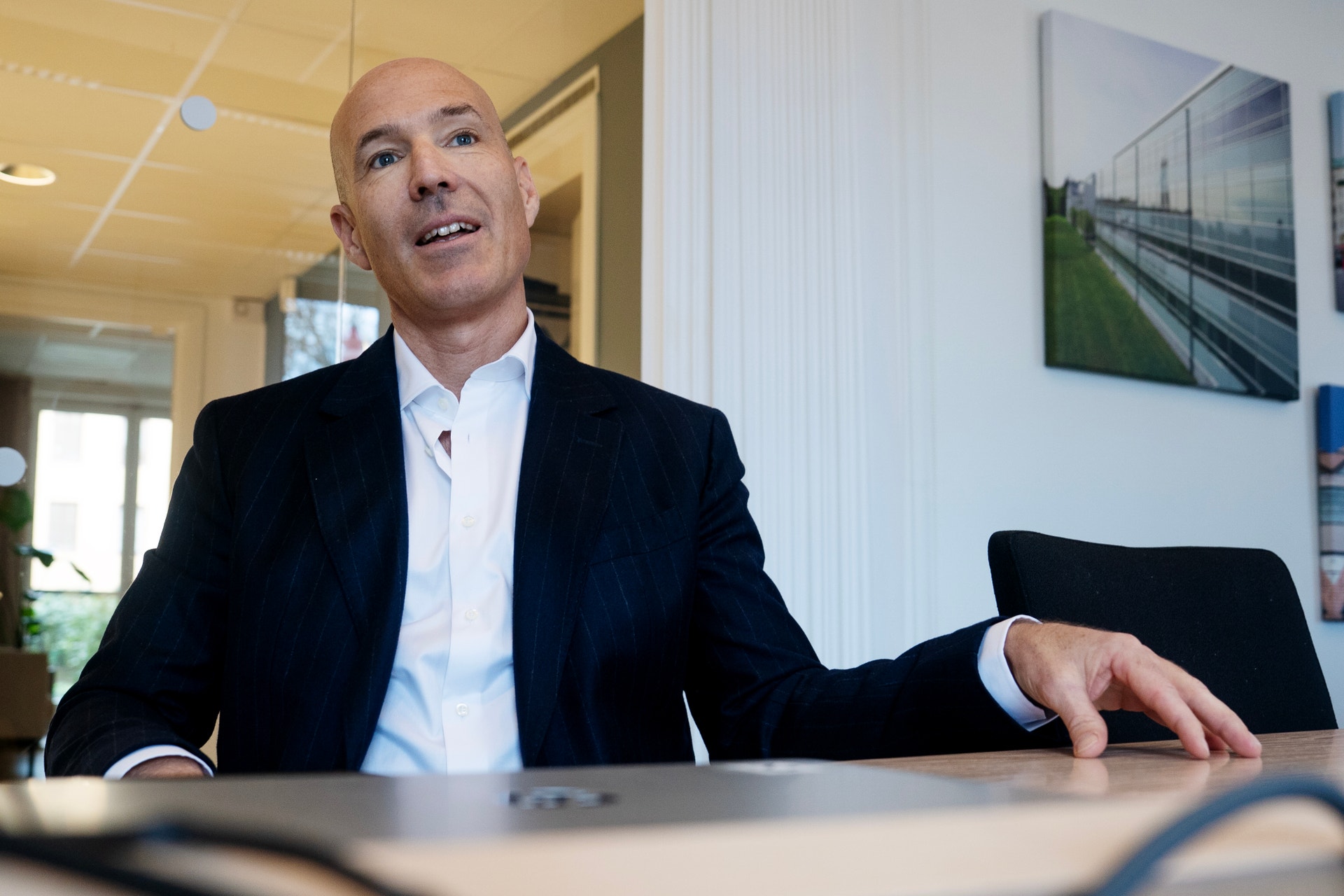 Porträtt av en man i svart kostym och vit skjorta som sitter vid ett skrivbord på ett kontor.