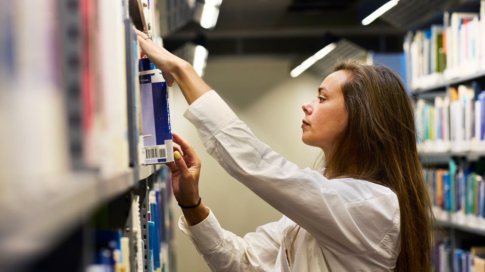 Julia Ravanis står och bläddrar man böcker i ett gammalt arkiv. 