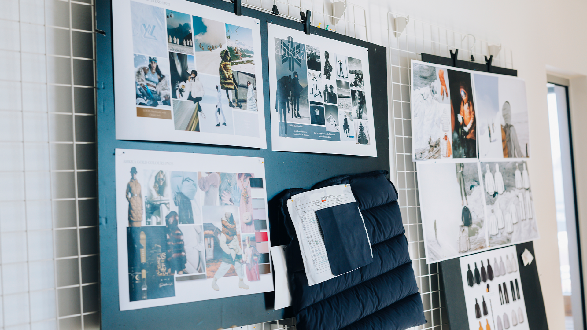 En vägg med en moodboard fylld med utskrivna fotografier, designskisser och inspirationsmaterial organiserat på blå och vita paneler.