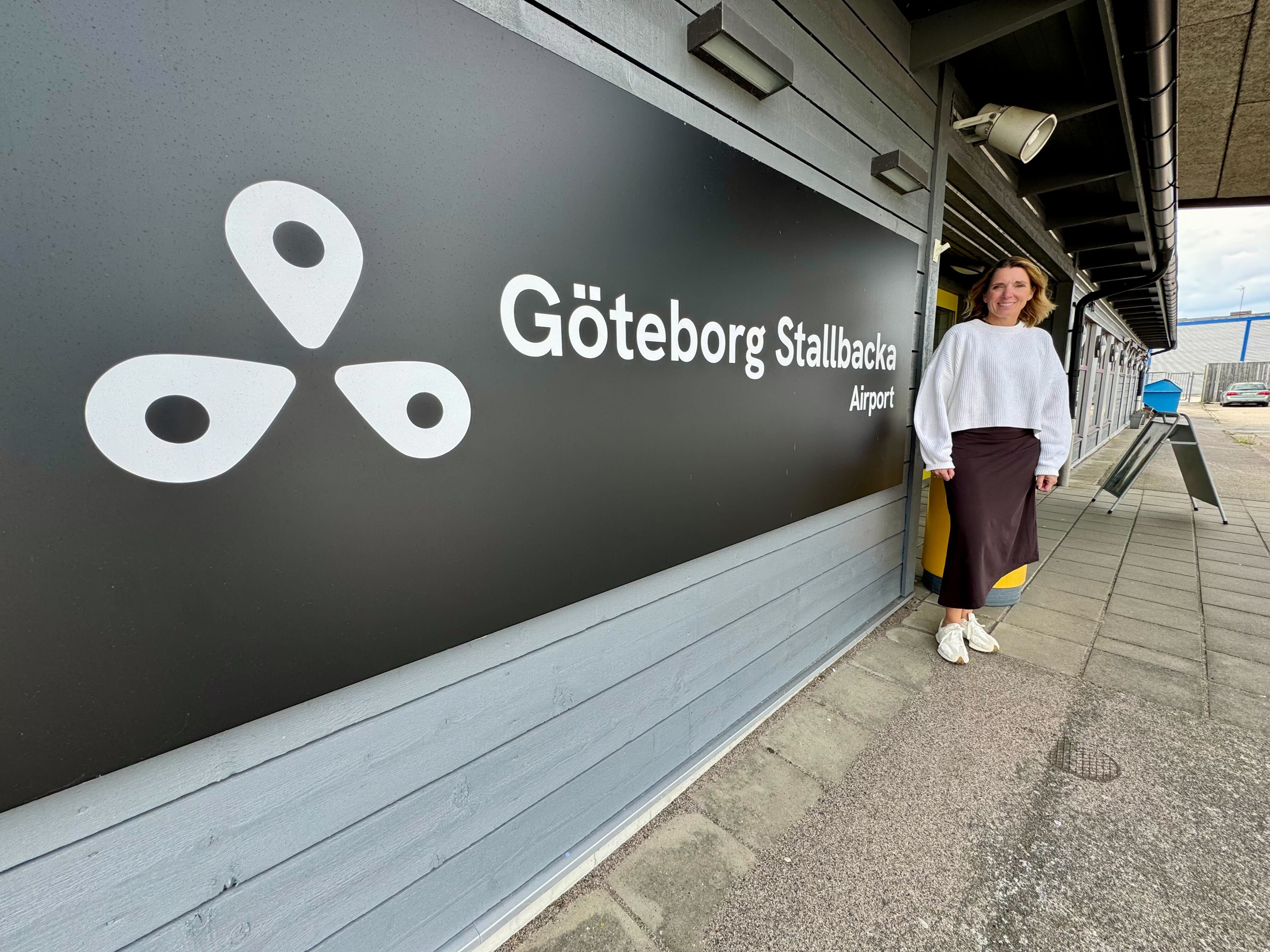 En person står vid en skylt för Göteborg Stallbacka Airport med vit logotyp och text på mörkgrå vägg.