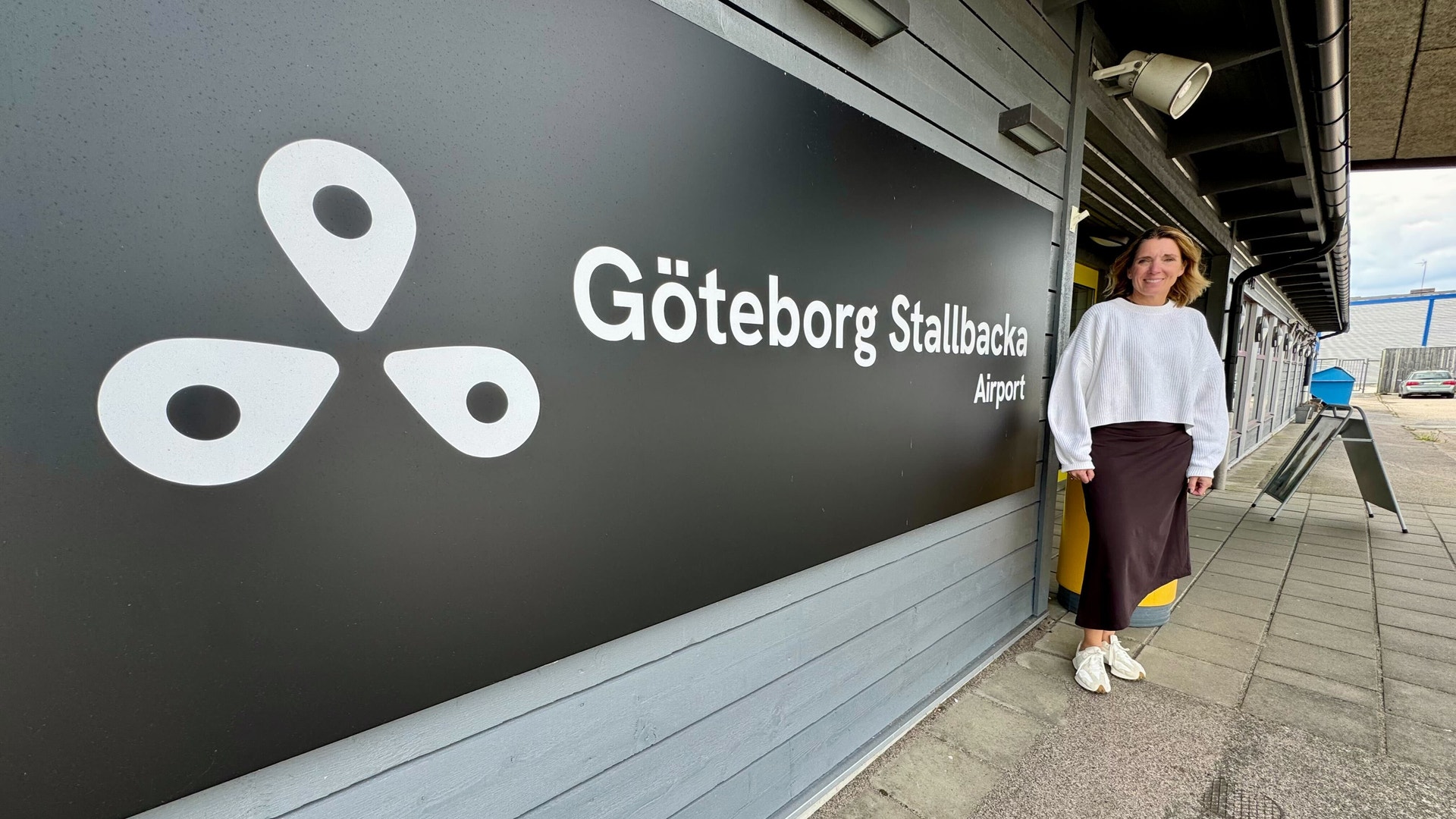 En person står vid en skylt för Göteborg Stallbacka Airport med vit logotyp och text på mörkgrå vägg.
