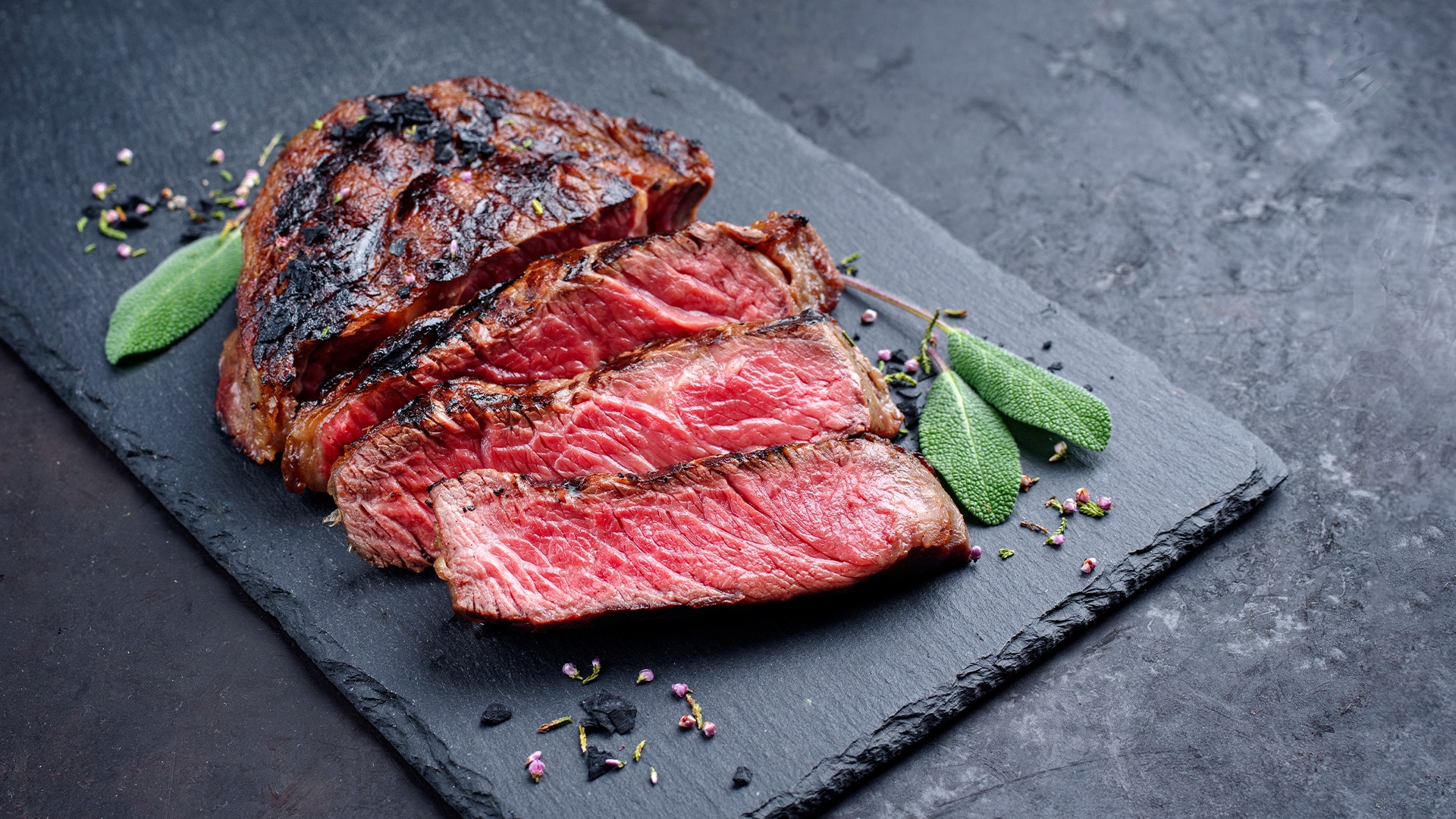 Grillad och skivad biff, mediumstekt, serverad på en mörk skiffertallrik med salviablad.