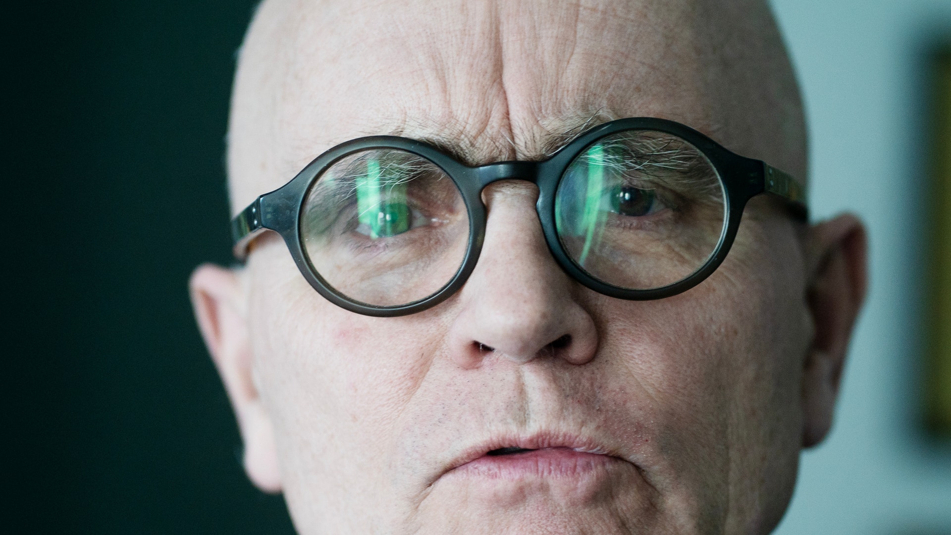Porträtt av en äldre man med runda svarta glasögon och reflexioner i glasen.