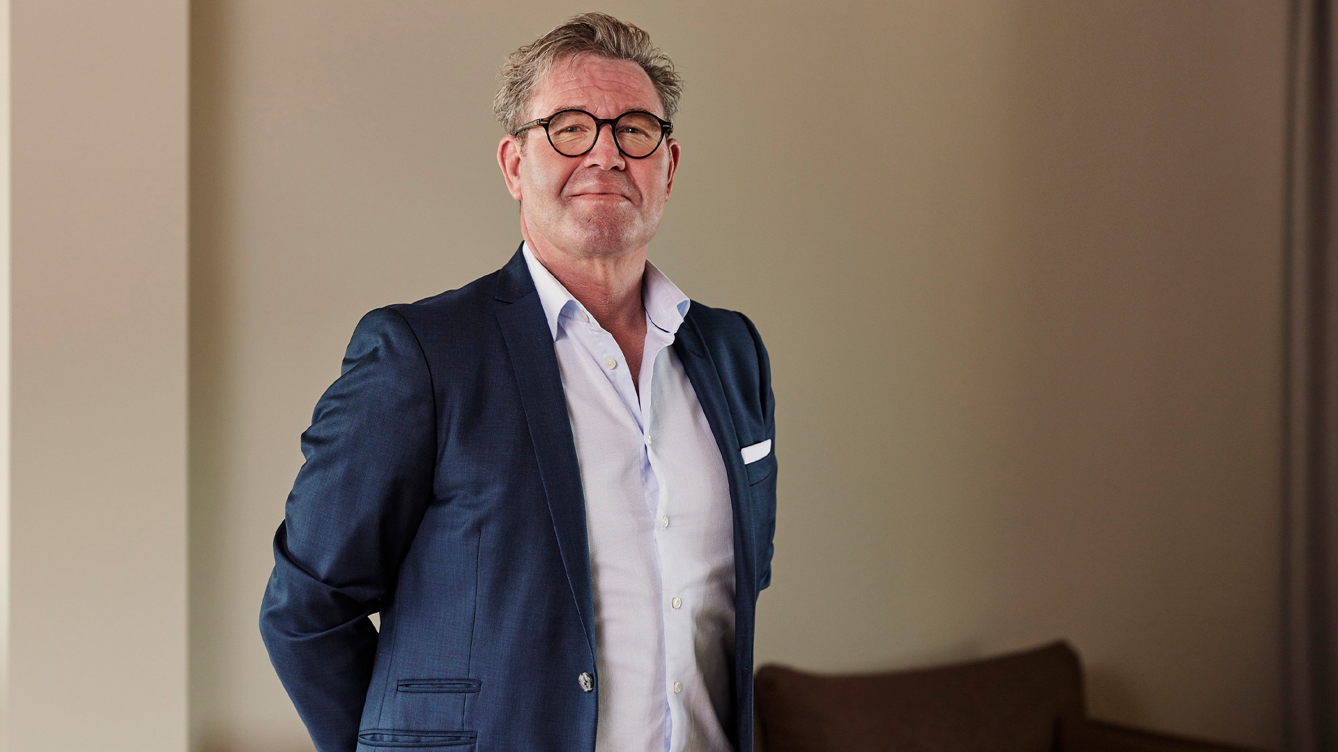 Porträttfoto av en man i marinblå kavaj och glasögon