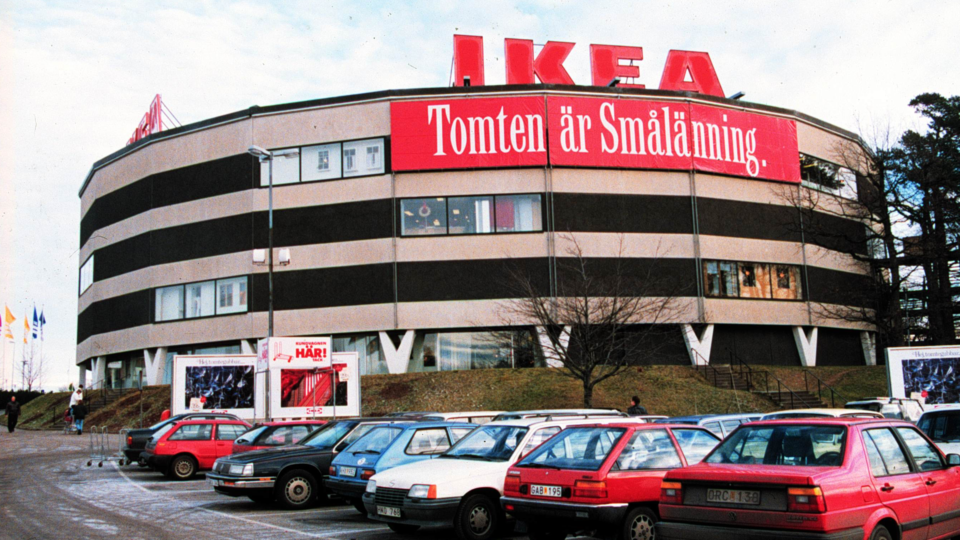 IKEA-butik med rundad arkitektur och röd skylt. Flera bilar parkerade framför byggnaden.