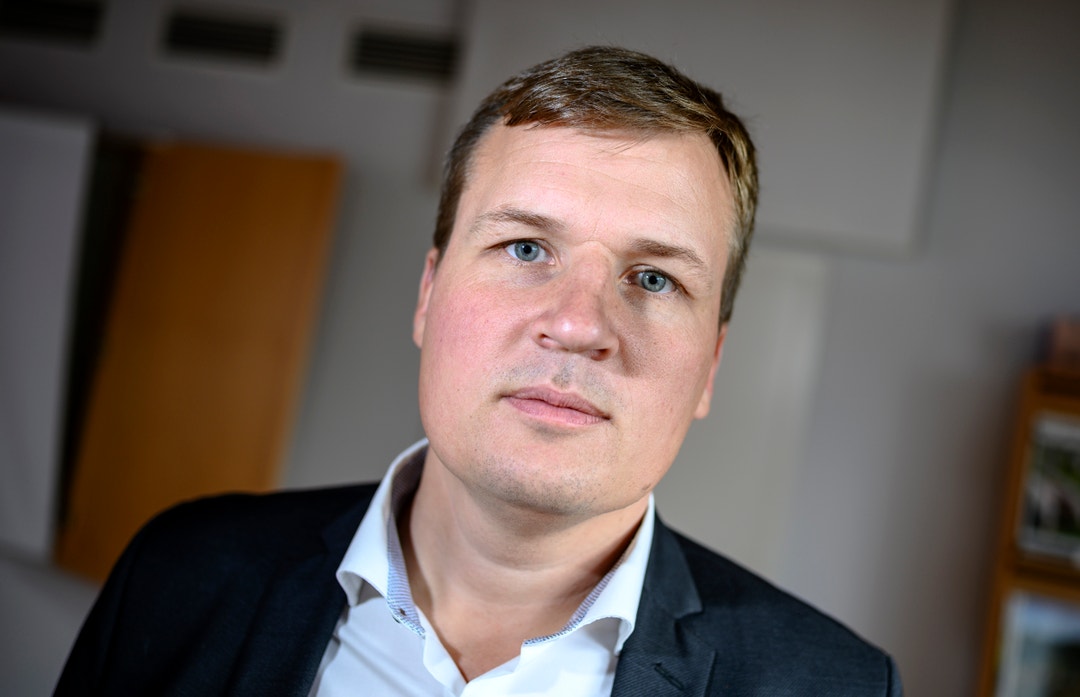 Porträtt av en man i mörk kavaj och ljus skjorta i en inomhusmiljö.