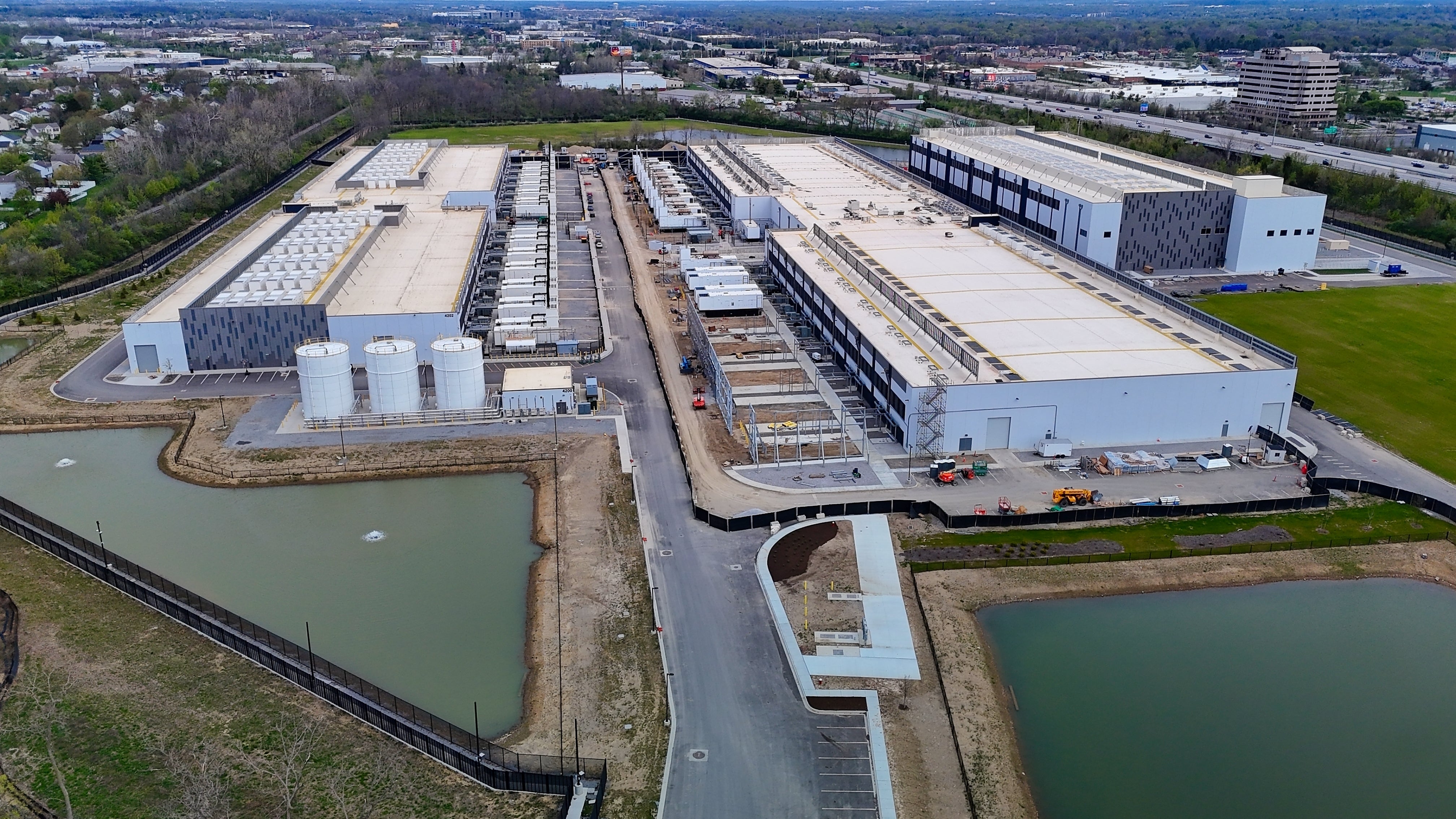 Flygbild över ett stort industriområde med flera vita byggnader, kylanläggningar och två dammar, omgivet av vägar och grönska.