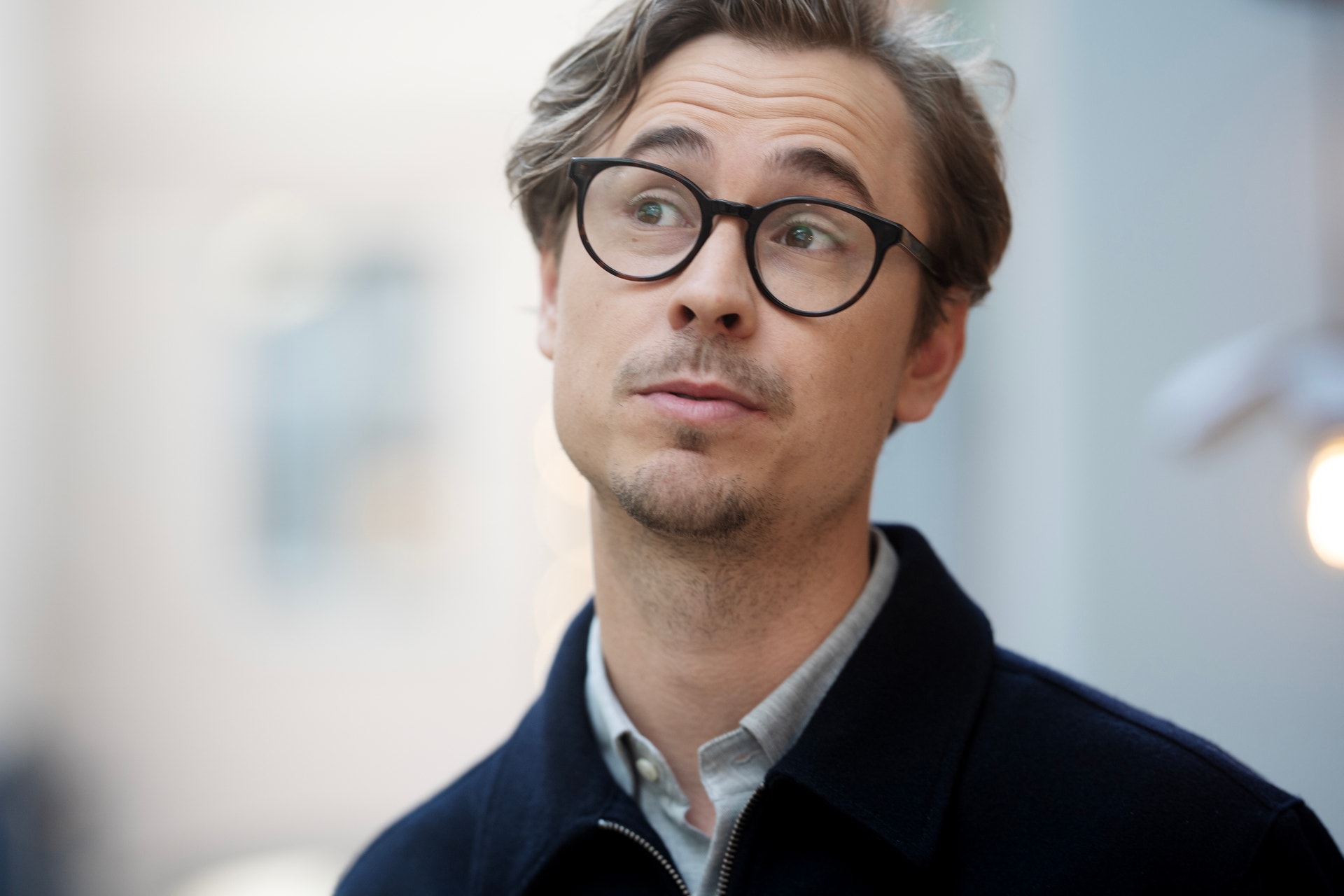 Porträtt av en man med glasögon och mörk jacka mot suddig bakgrund.