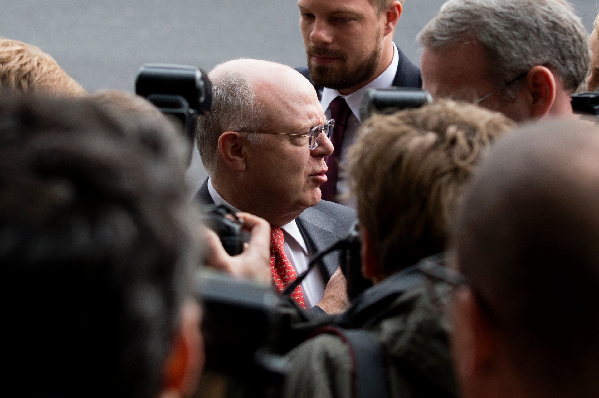Man i kostym omgiven av journalister med mikrofoner och kameror vid en presskonferens.
