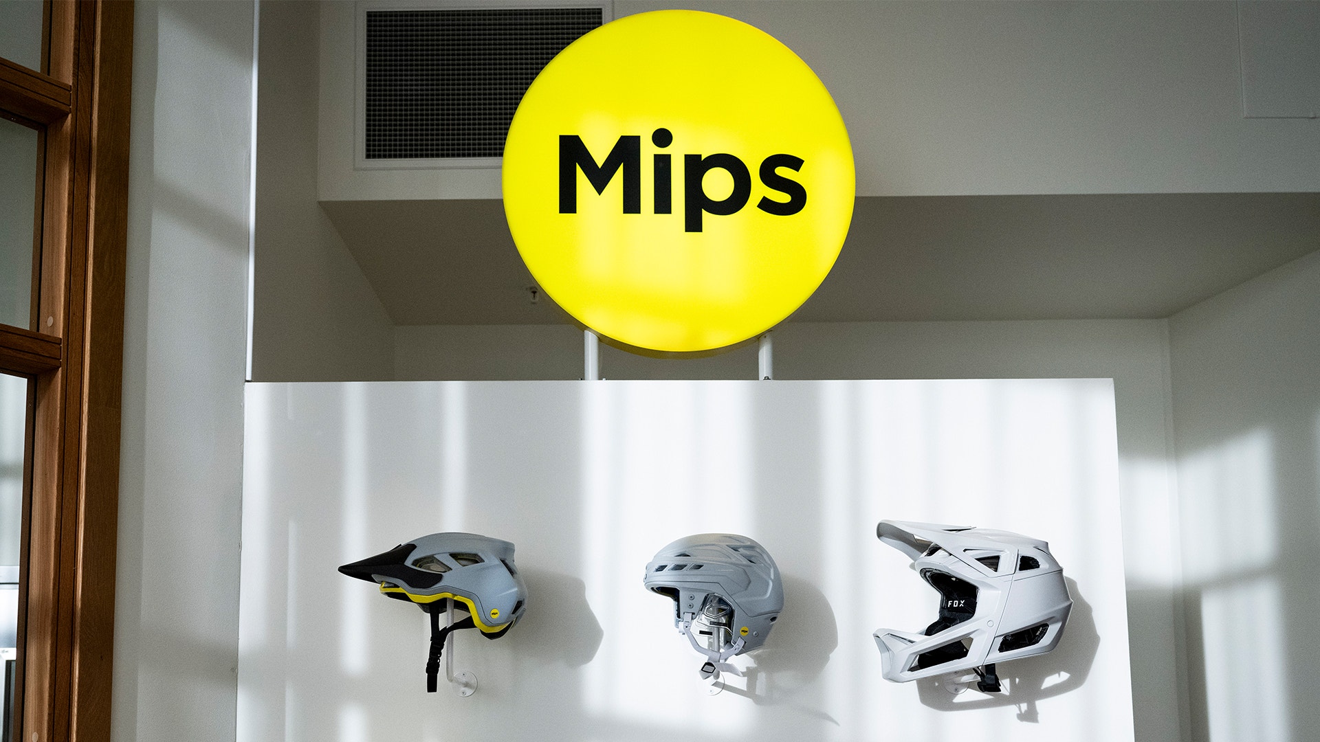 Tre cykelhjälmar monterade på en vägg under en gul cirkel märkt Mips, som visar olika hjälmmodeller för säkerhet vid cykling.