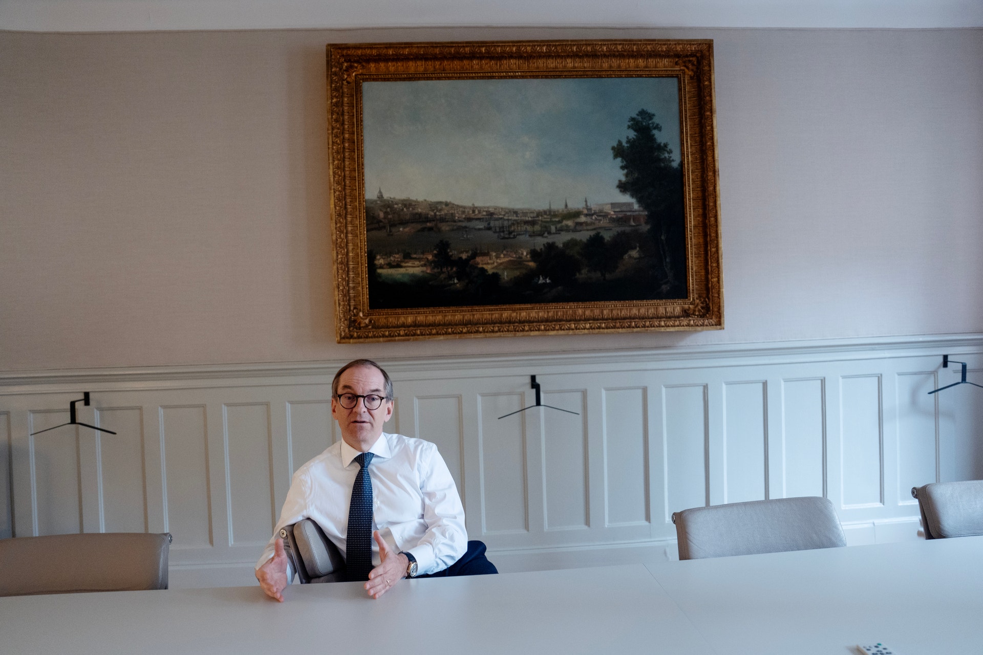 Porträttfoto av en man i vit skjorta och mörkblå slips som sitter vid ett bord i ett modernt kontor.