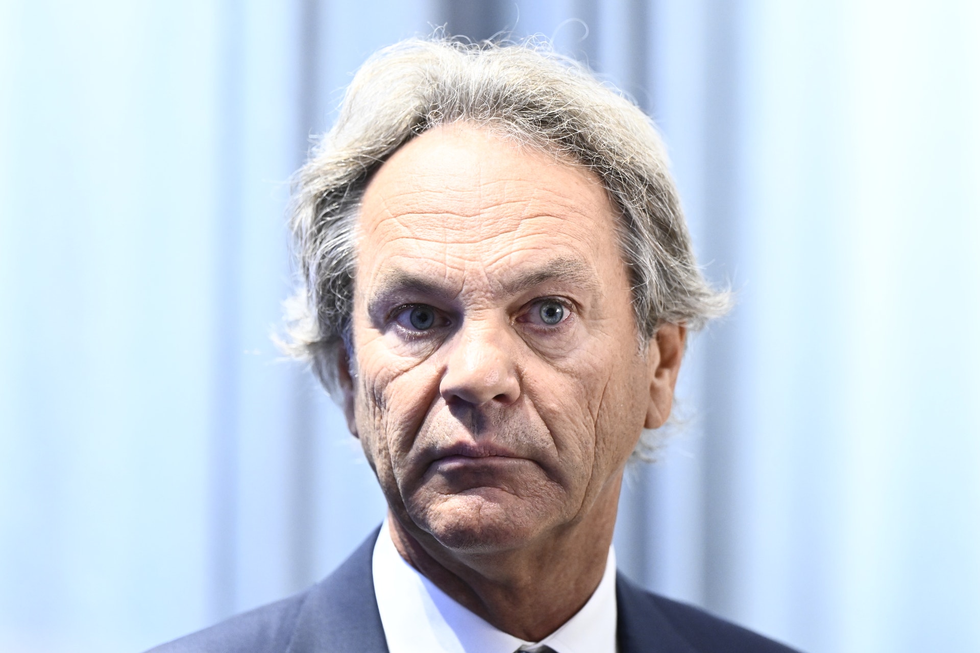 Porträtt av en äldre man med grått hår, klädd i mörk kostym och slips.