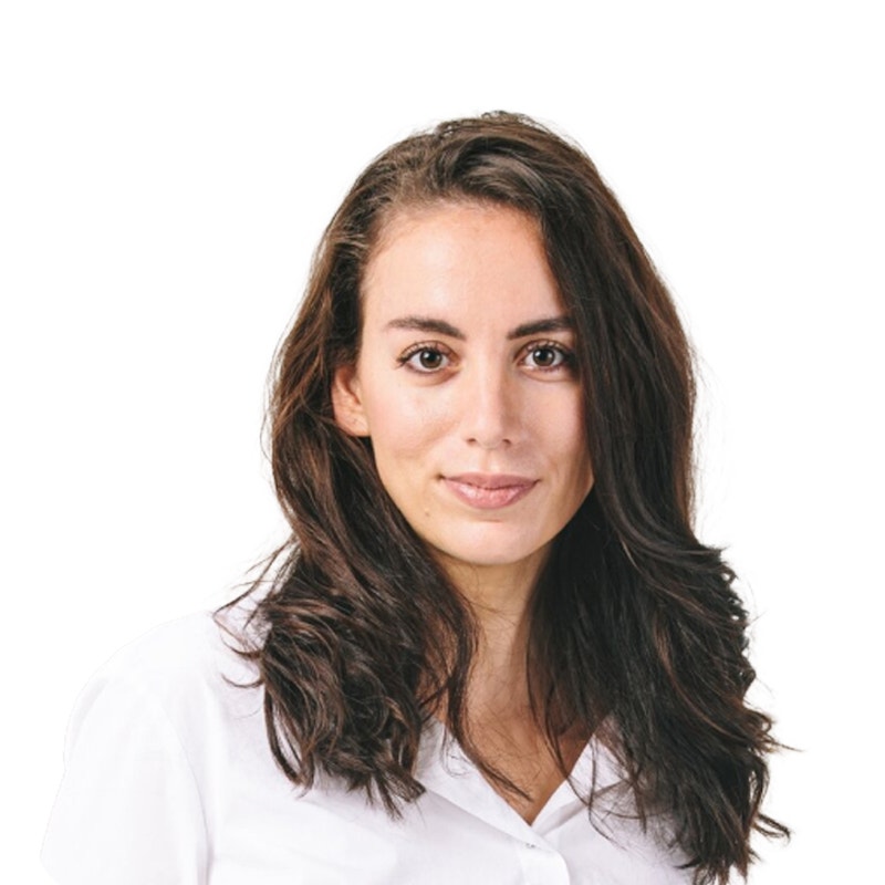 Porträttfoto av en kvinna med långt mörkt hår, klädd i vit skjorta mot vit bakgrund.