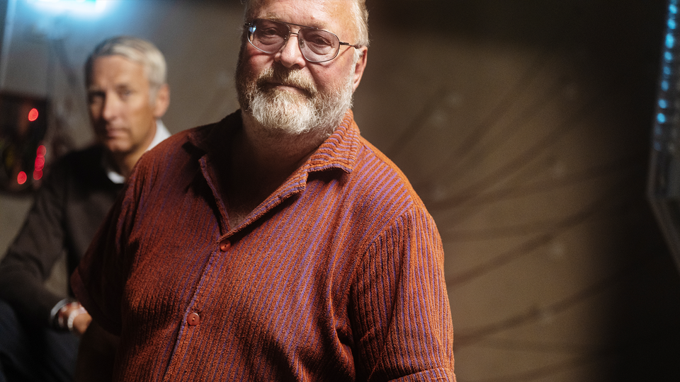 Jan Broman nere i källaren där Dino byggs. Han har på sig en rödskalig skjorta och metalliska glasögon.