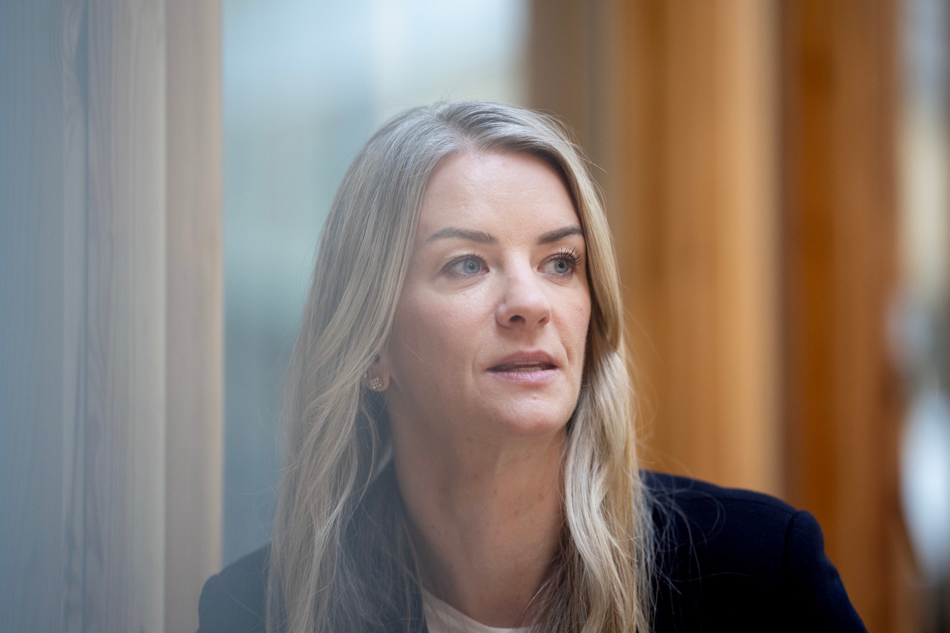 Porträtt av en kvinna med långt blont hår, iklädd mörk klädsel, fotograferad inomhus.