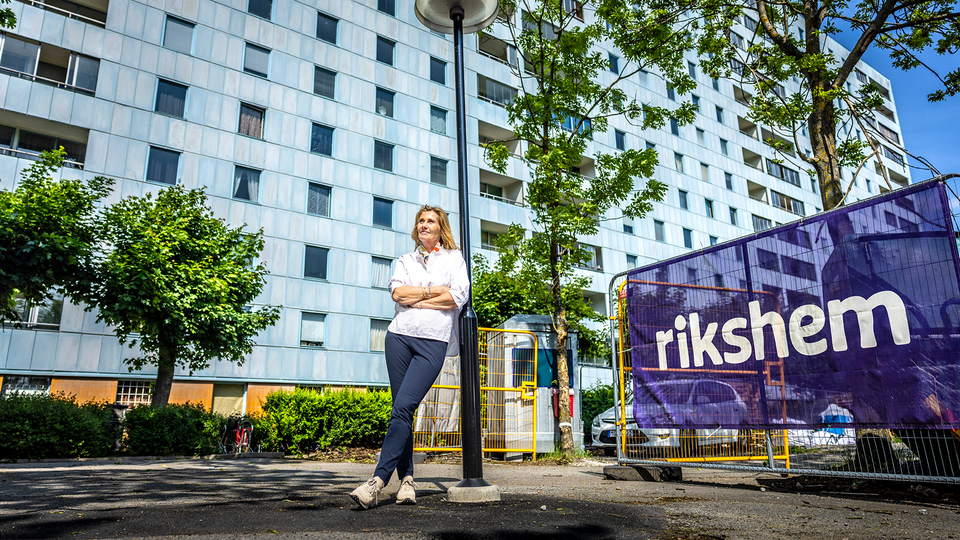 Anette Frumerie står och lutar sig mot en lyktstolpe framför Rikshems fasader.