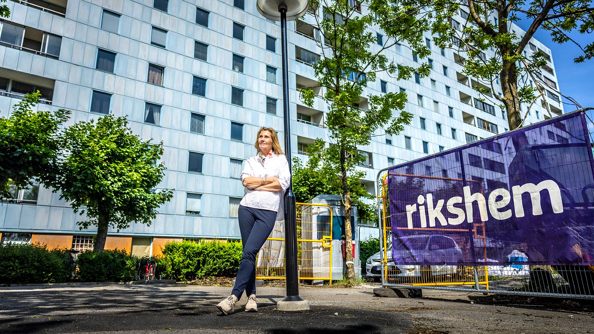 Anette Frumerie står och lutar sig mot en lyktstolpe framför Rikshems fasader.