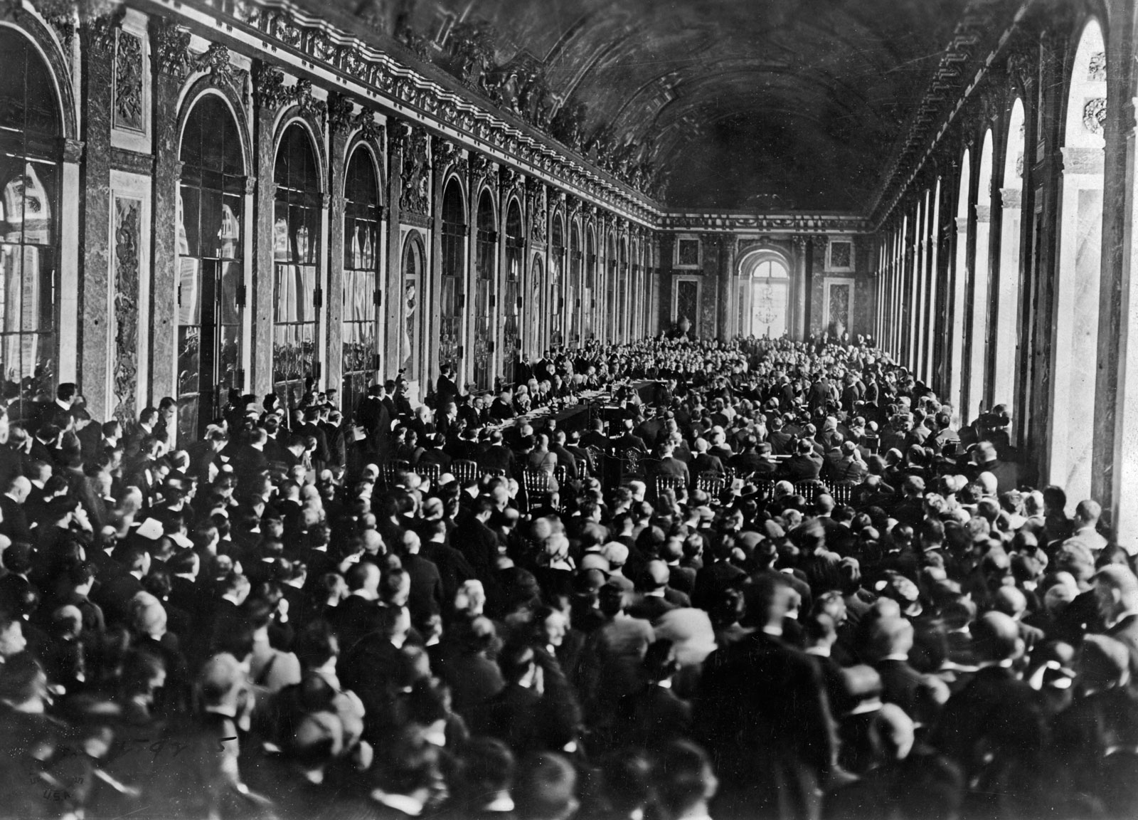 Svartvitt historiskt foto av en stor folksamling i en praktfull sal där Versaillesfördraget undertecknas.