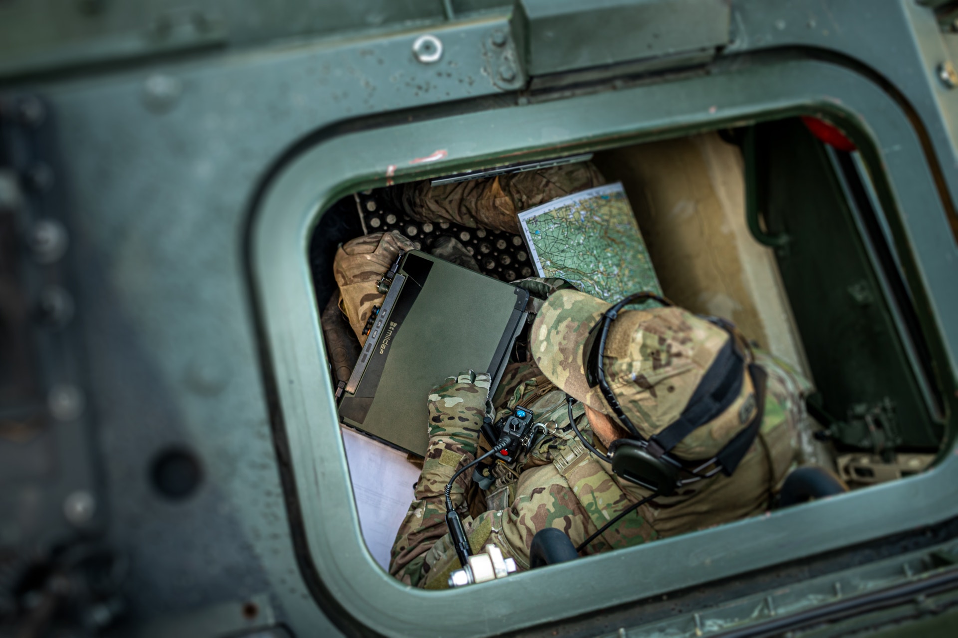 Soldat i militär uniform och utrustning sedd uppifrån genom en öppen lucka på ett militärfordon.