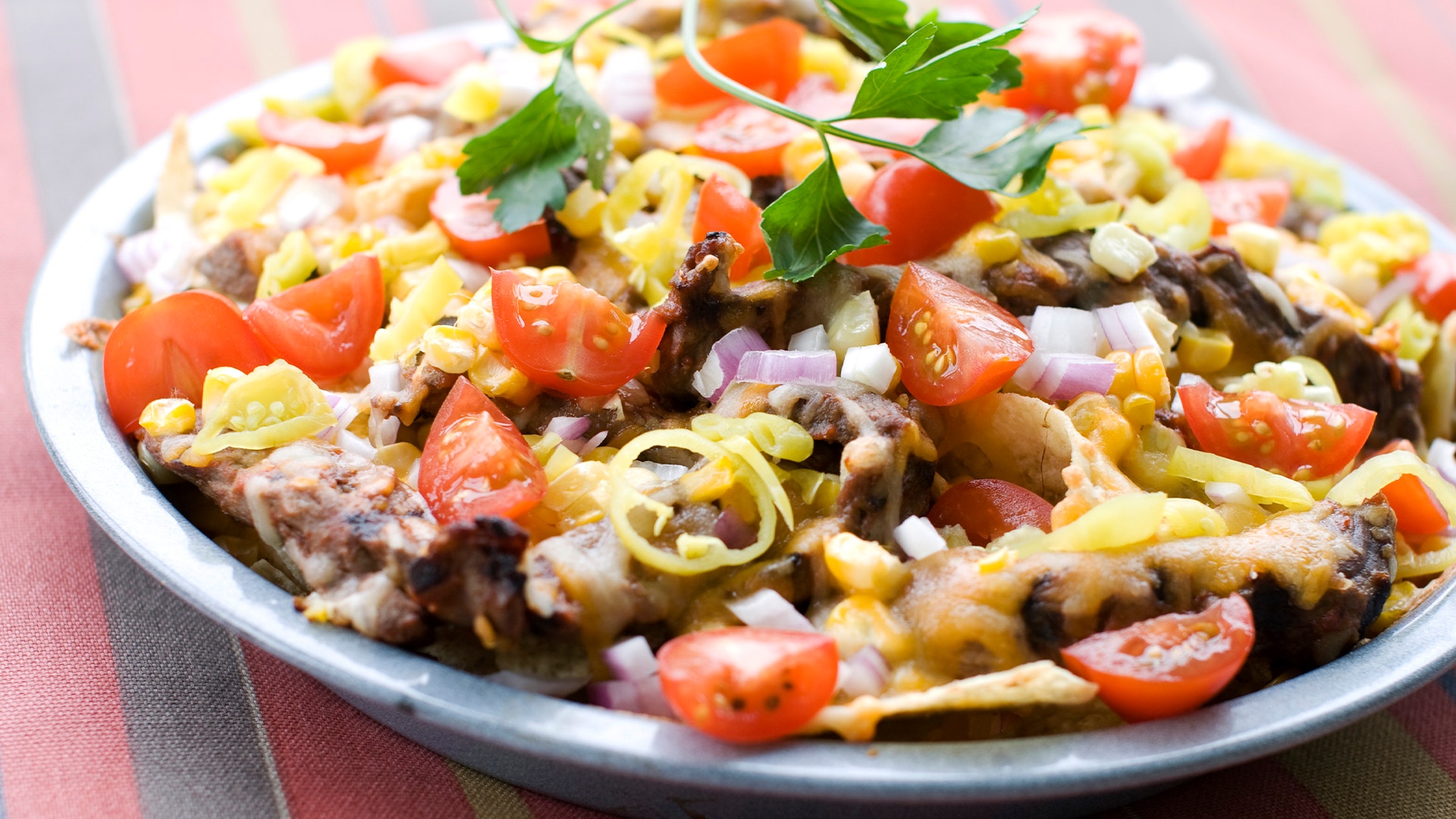 En tallrik med nachos toppad med köttfärs, röd paprika, gul lök, majs och grön koriander.