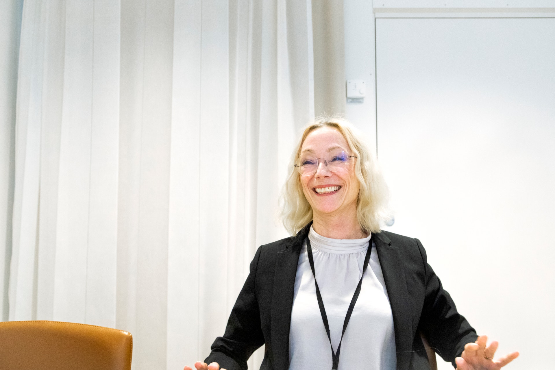 En kvinna presenterar och gestikulerar med händerna. Hon bär glasögon, svart blazer och har blont hår.