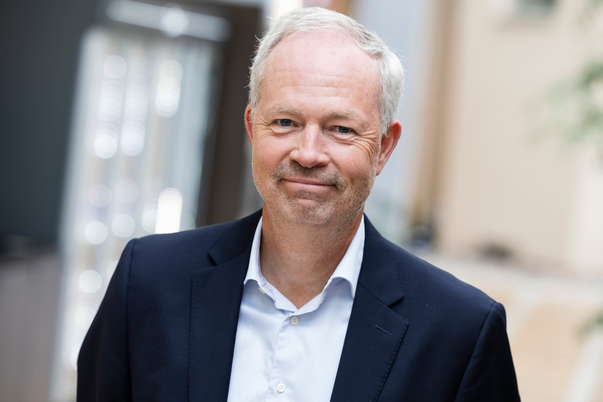 Porträtt av en man med grått hår, iklädd mörkblå kavaj och vit skjorta.